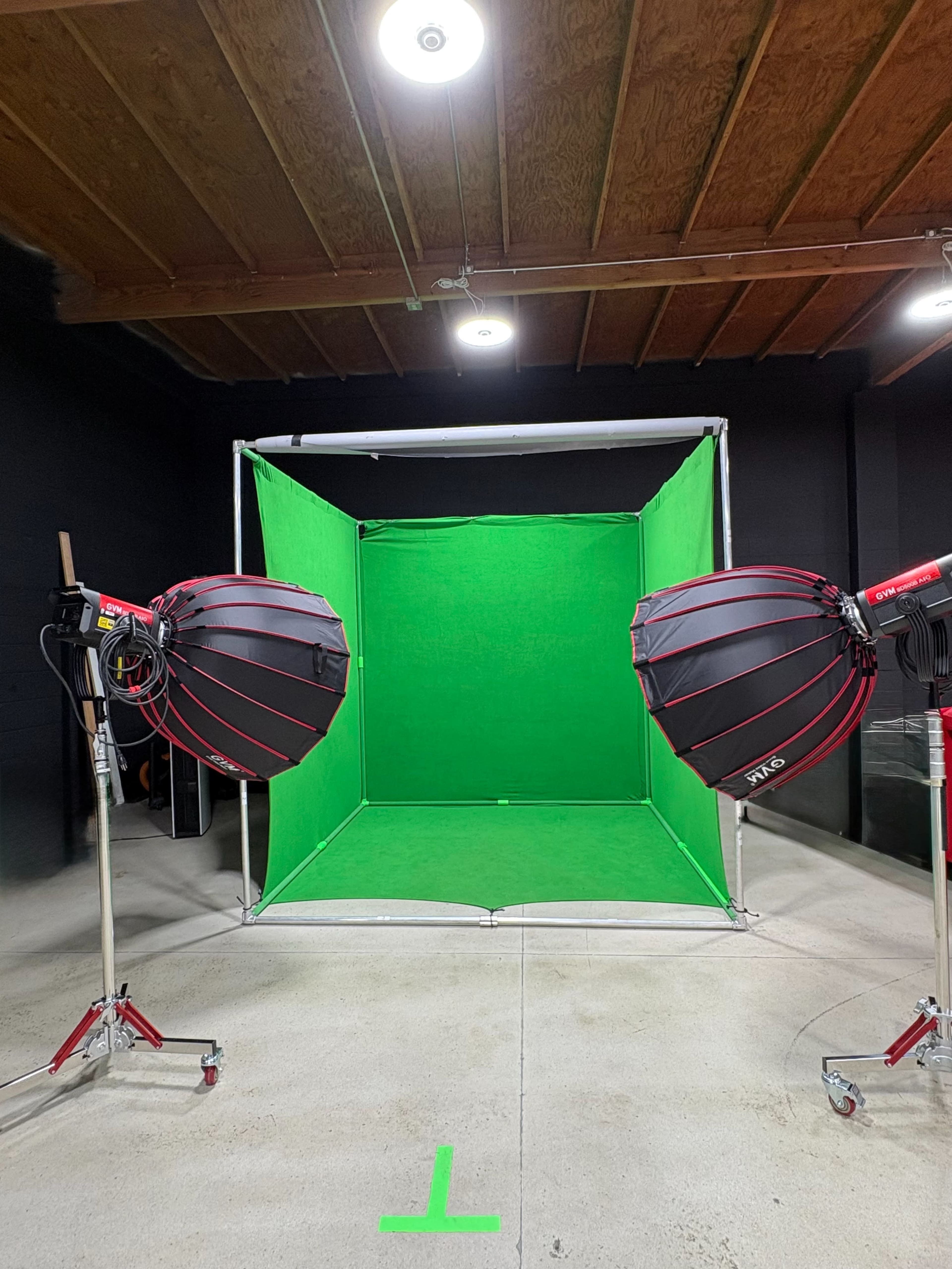 The image shows a studio setup with a green screen backdrop framed by two large softbox lights on stands.