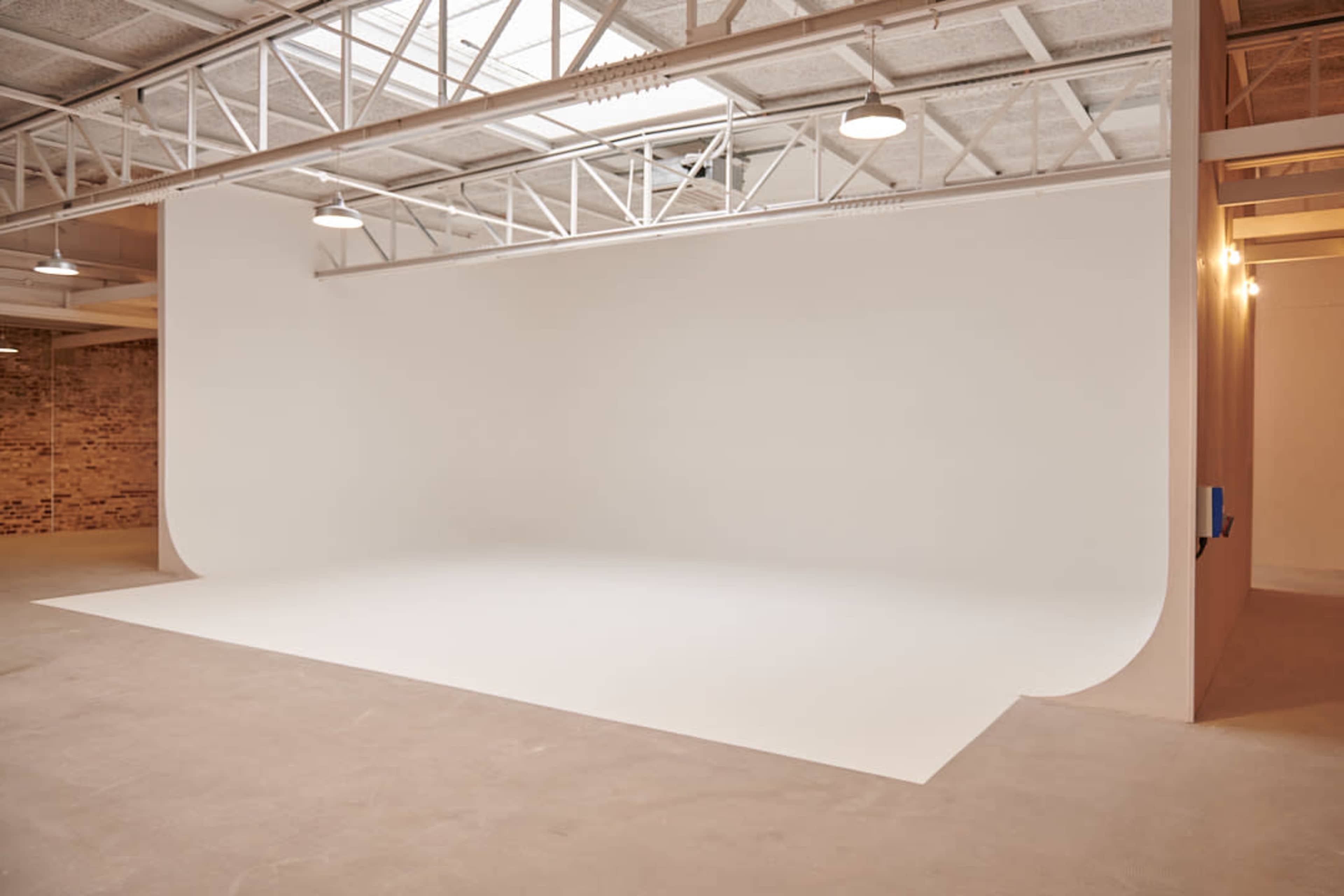 The image shows a spacious, empty photography studio with a seamless white backdrop and concrete floor.
