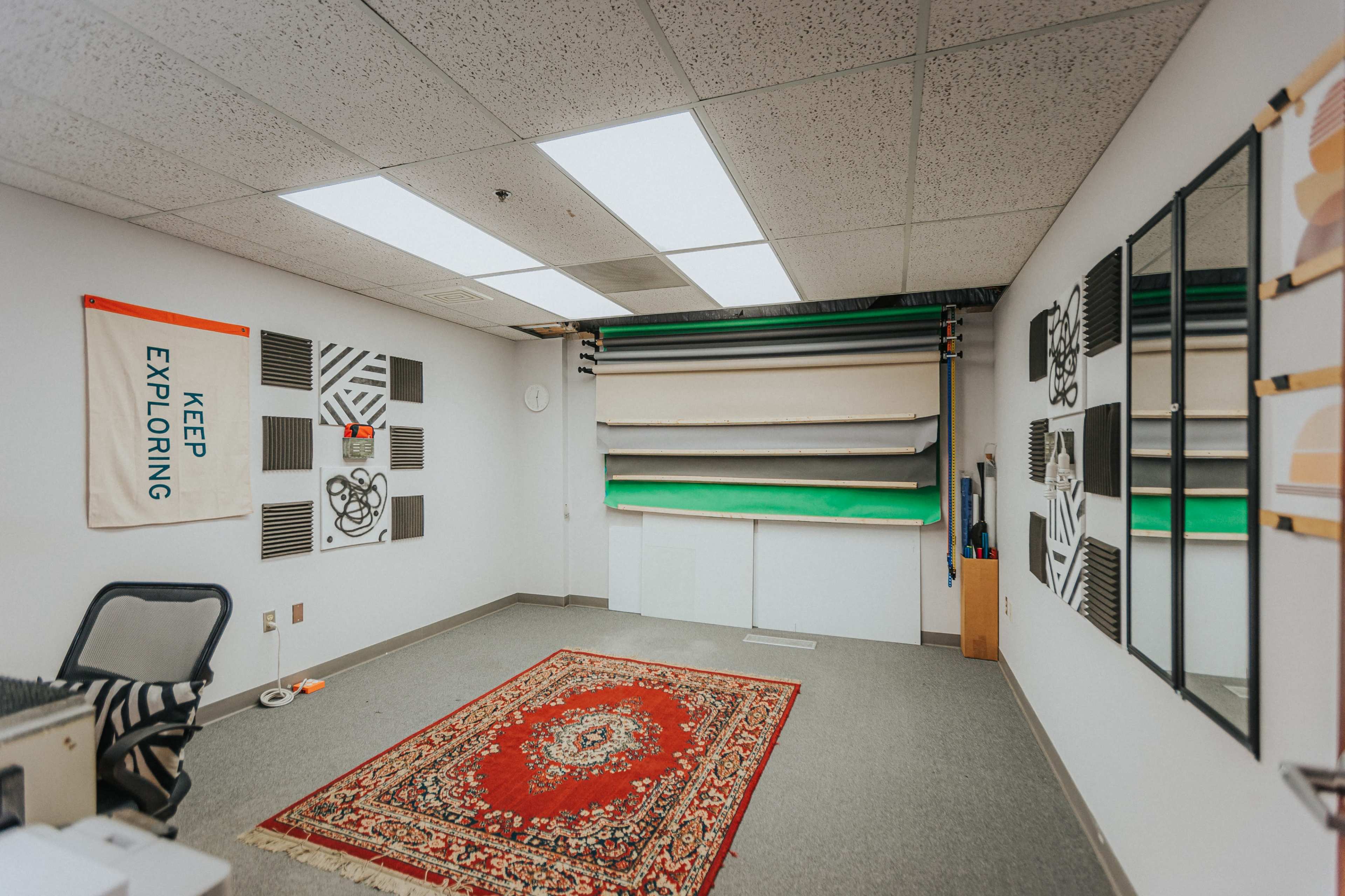A spacious studio room with a patterned area rug, large mirrors, and a backdrop setup consisting of colored rolls.