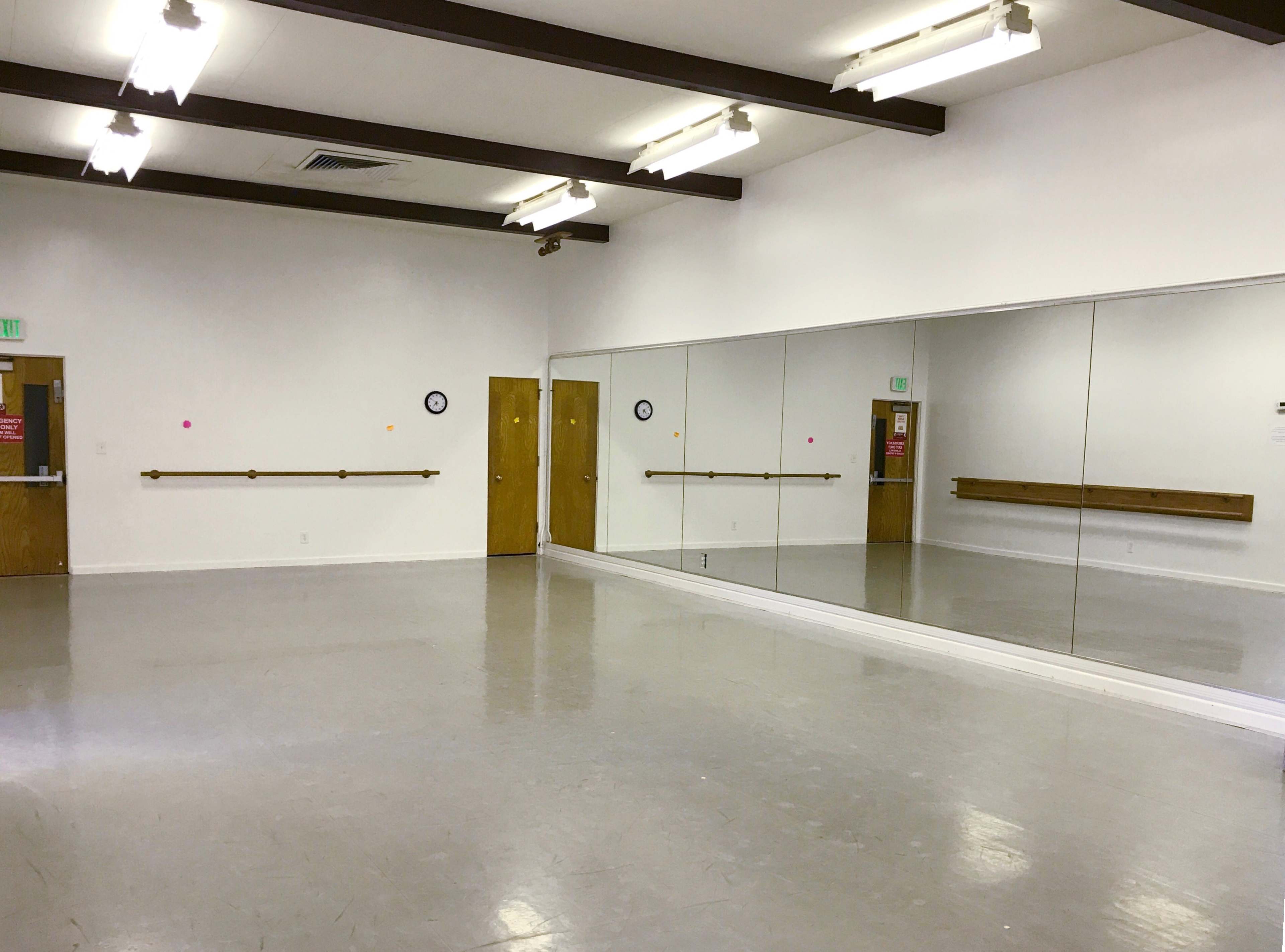 A spacious dance studio with mirrored walls, wooden barre, and two doors.