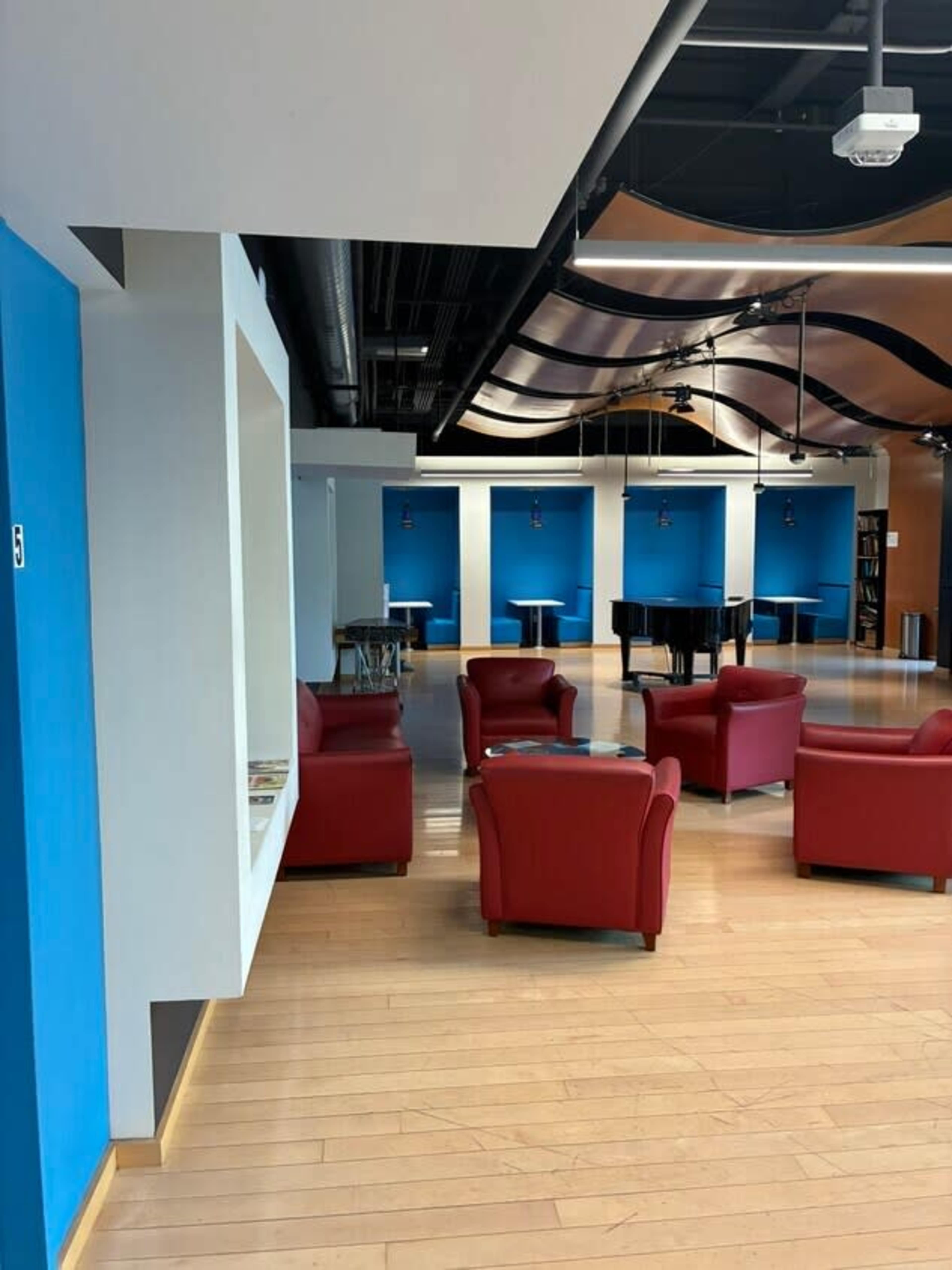 The image shows a modern interior space with red chairs and blue walls, featuring a piano in the background.