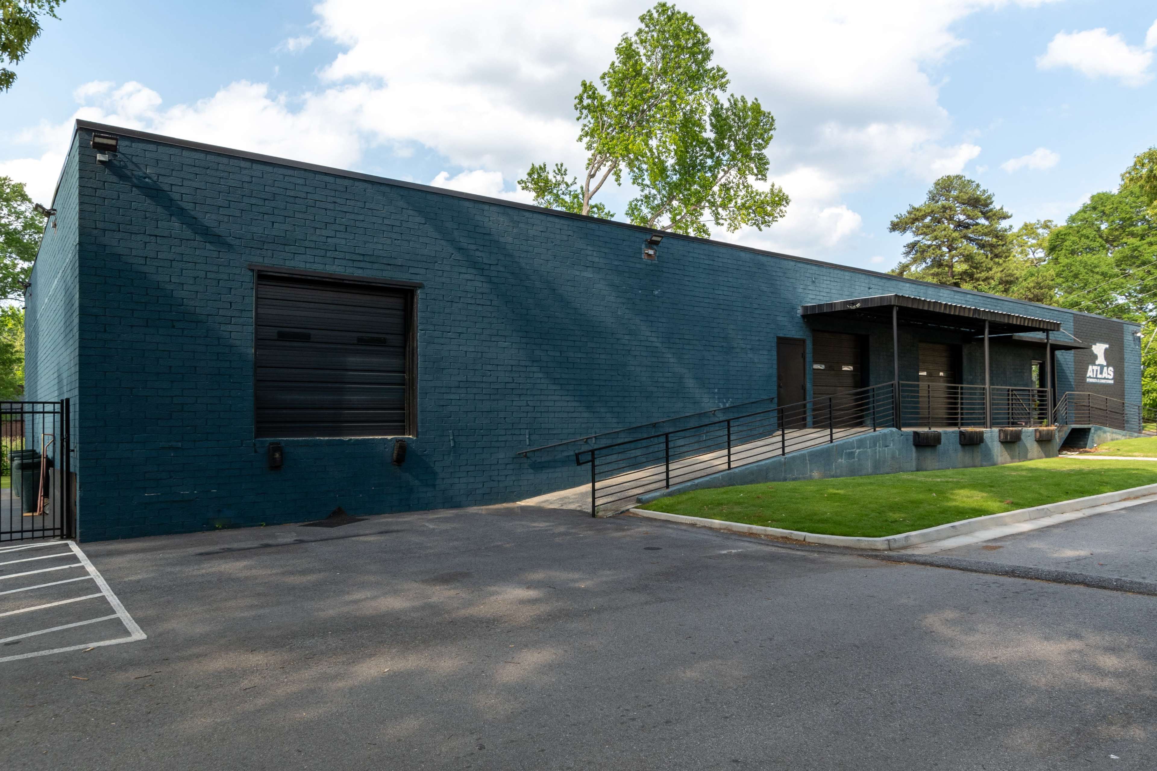 A dark blue, brick commercial building features a prominent entrance with a ramp and a fenced parking area.