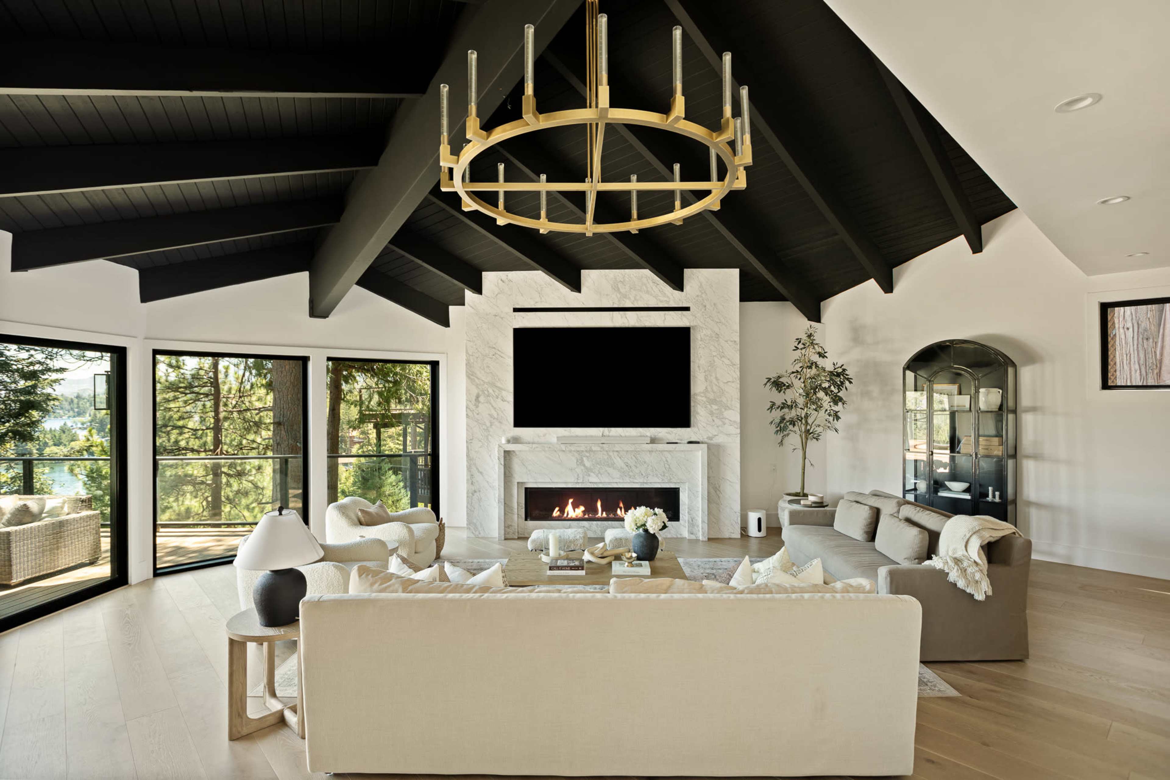 A spacious living room features high vaulted ceilings, a large stone fireplace, and modern furniture arranged around a central coffee table.