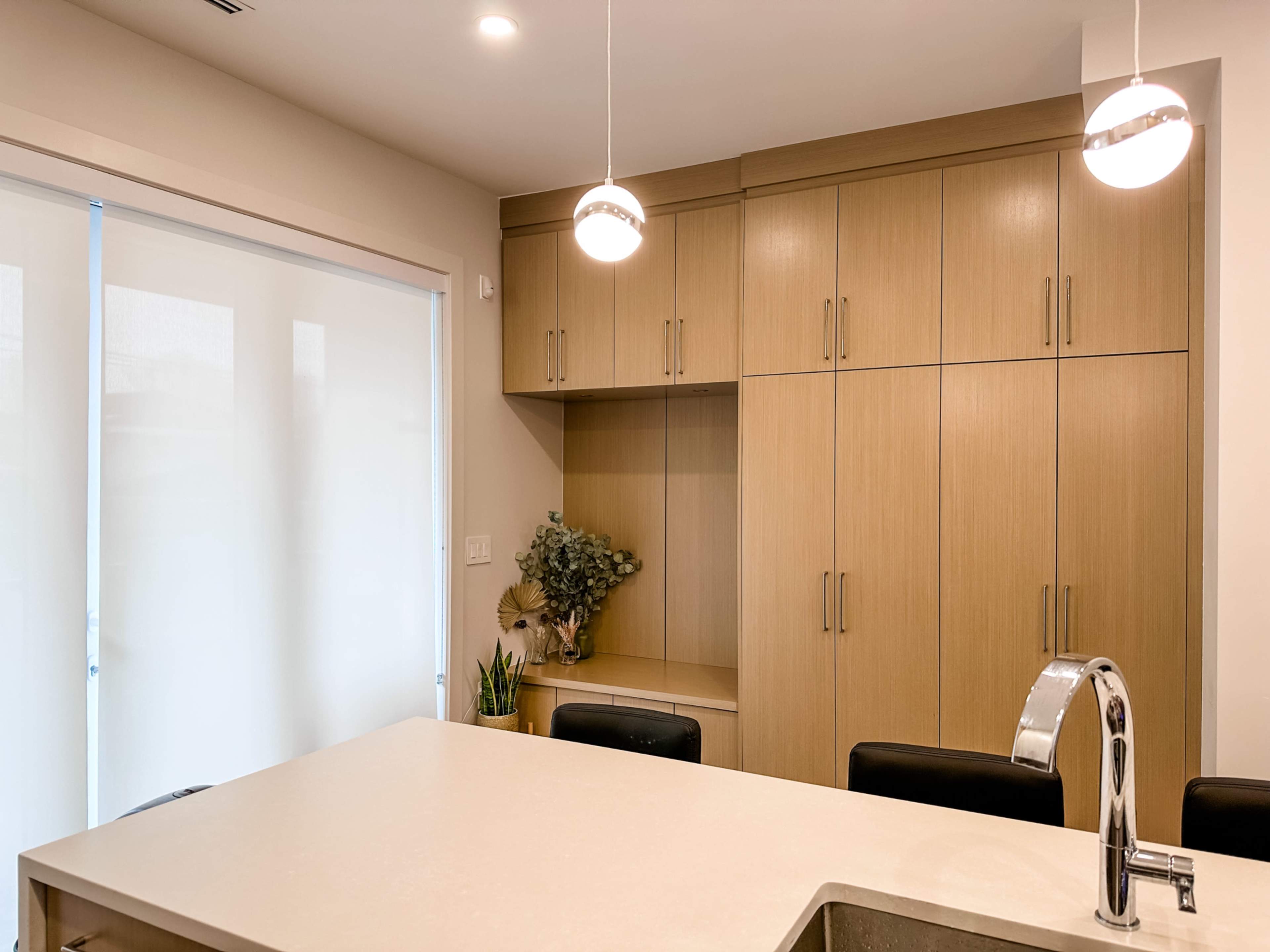 A modern kitchen features light wood cabinetry, a large white countertop, and pendant lighting above the island.