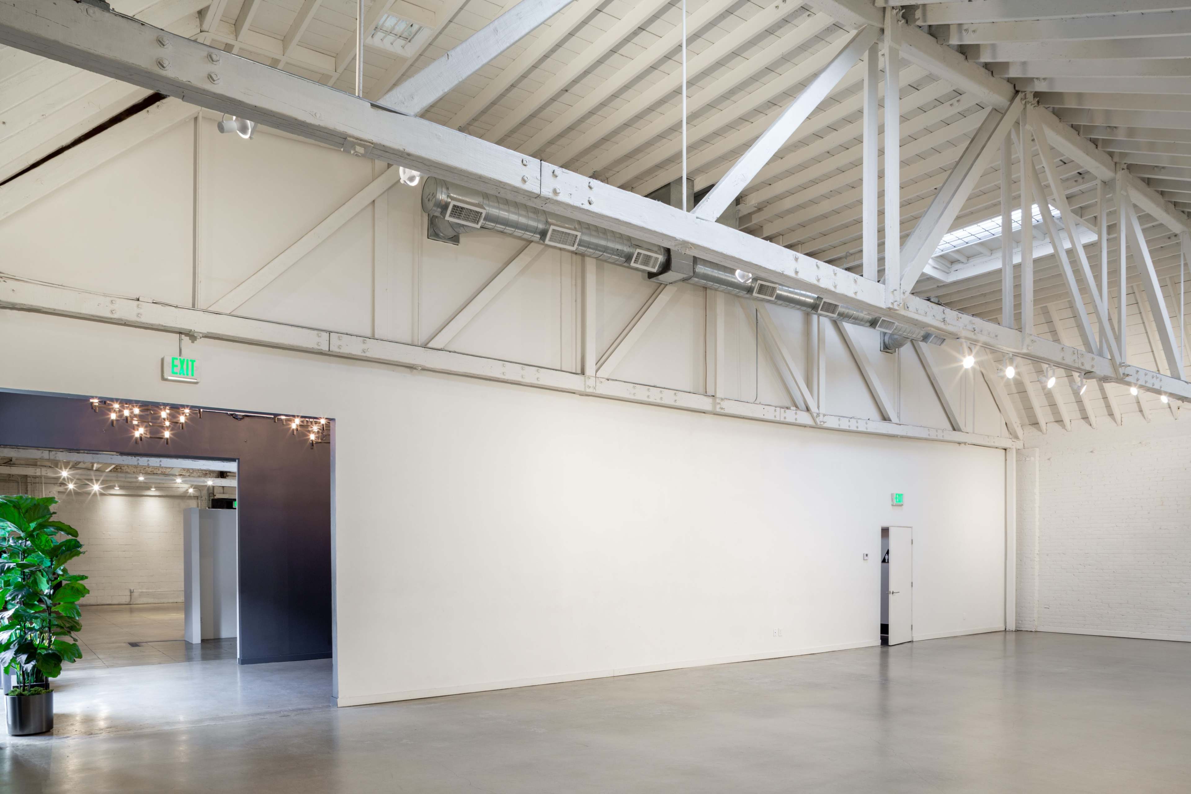 A spacious, empty interior of a modern industrial building features high ceilings, exposed beams, and a large wall painted white.