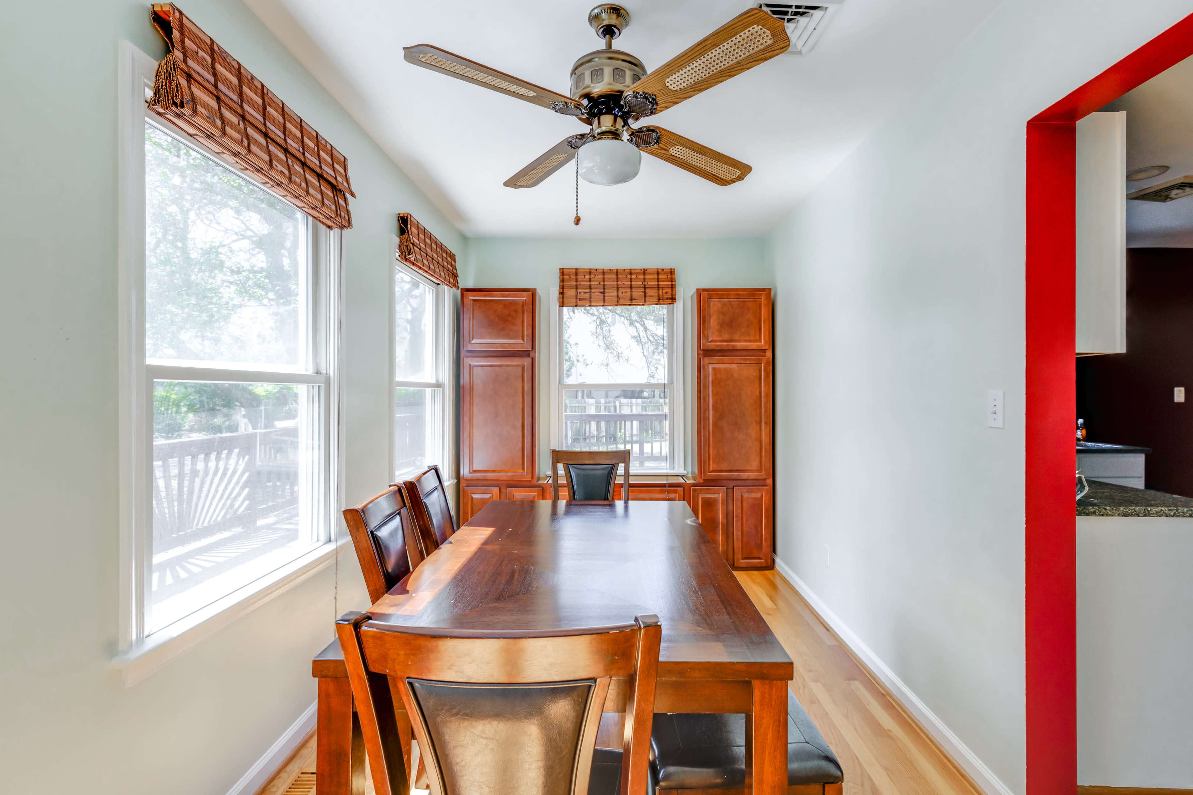 A dining area features a wooden table and chairs, with windows flanked by wooden blinds and cabinetry along the walls.