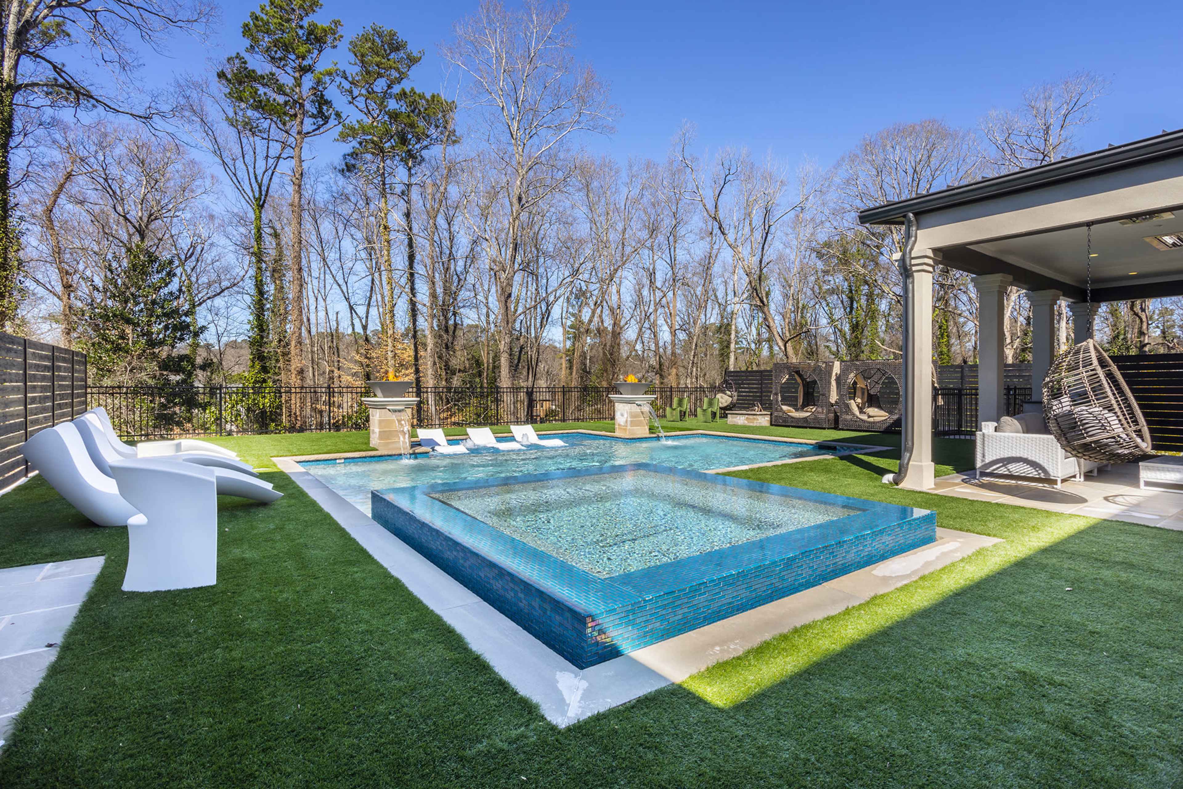 A rectangular swimming pool with a raised spa surrounded by green grass and lounge chairs in a wooded outdoor setting.