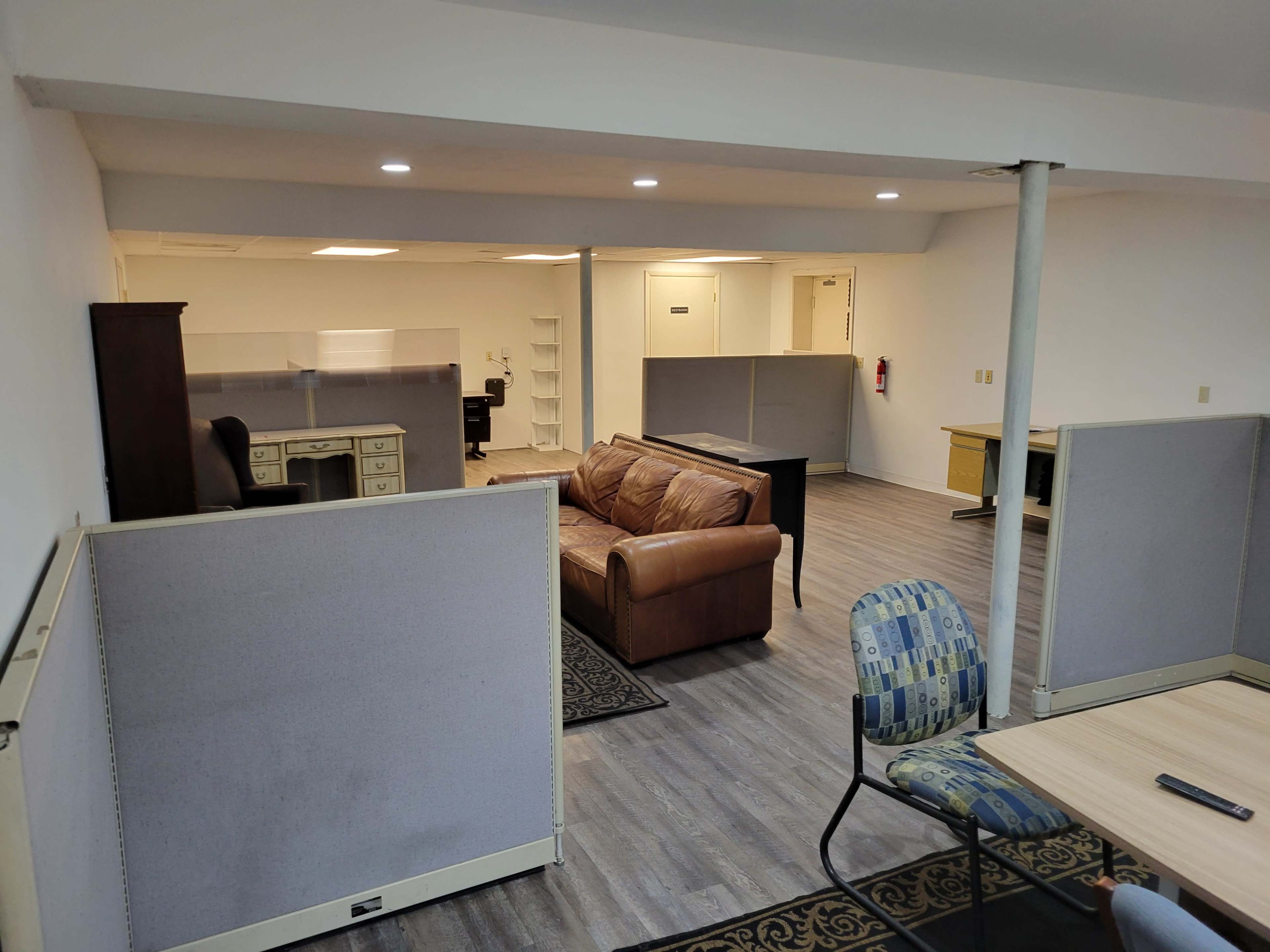 An office space featuring a brown couch, several desk areas, and partition dividers set on a wooden floor.