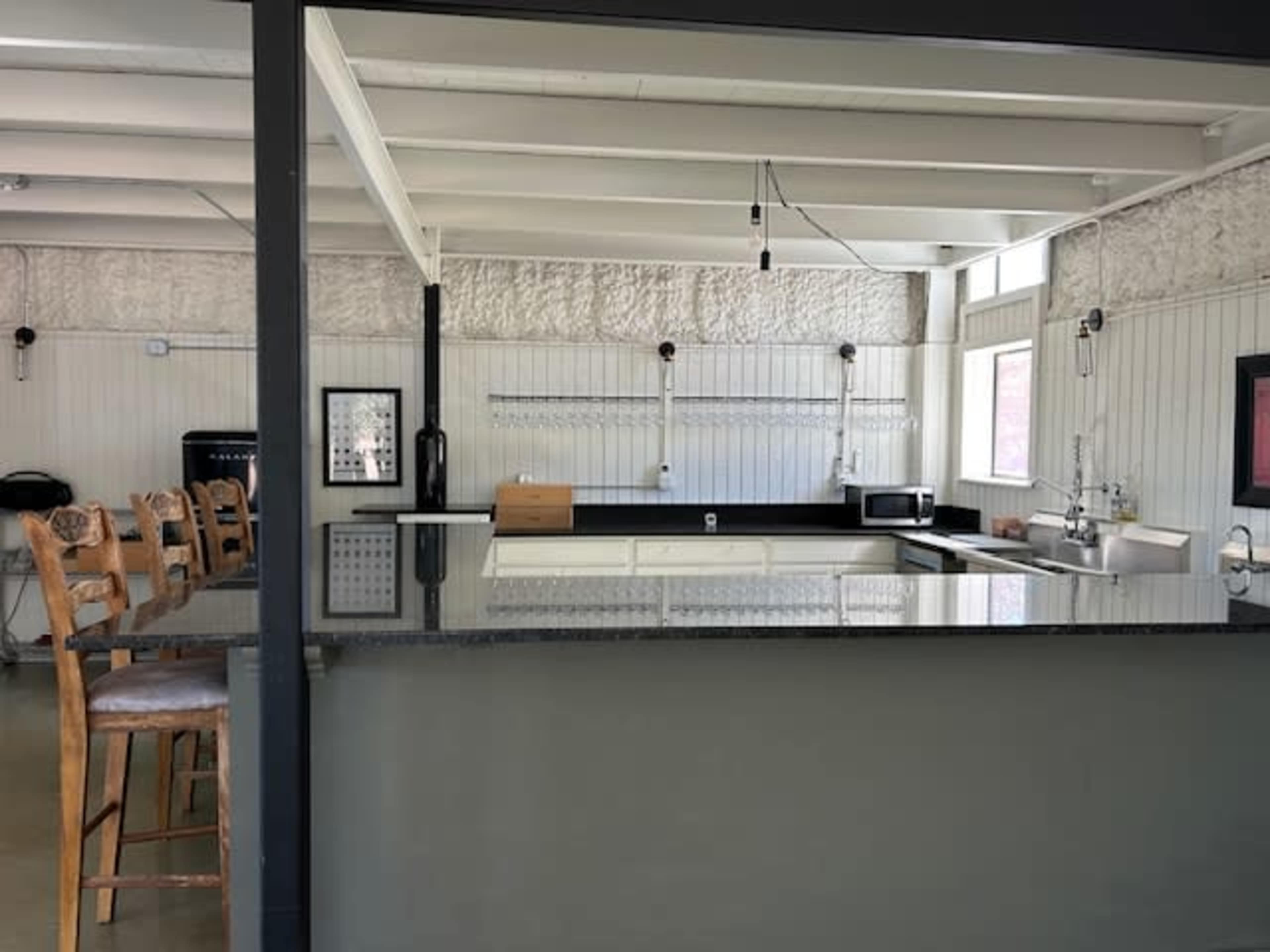 The image shows a modern kitchen with a bar counter, high chairs on one side, and various kitchen appliances on the countertops.