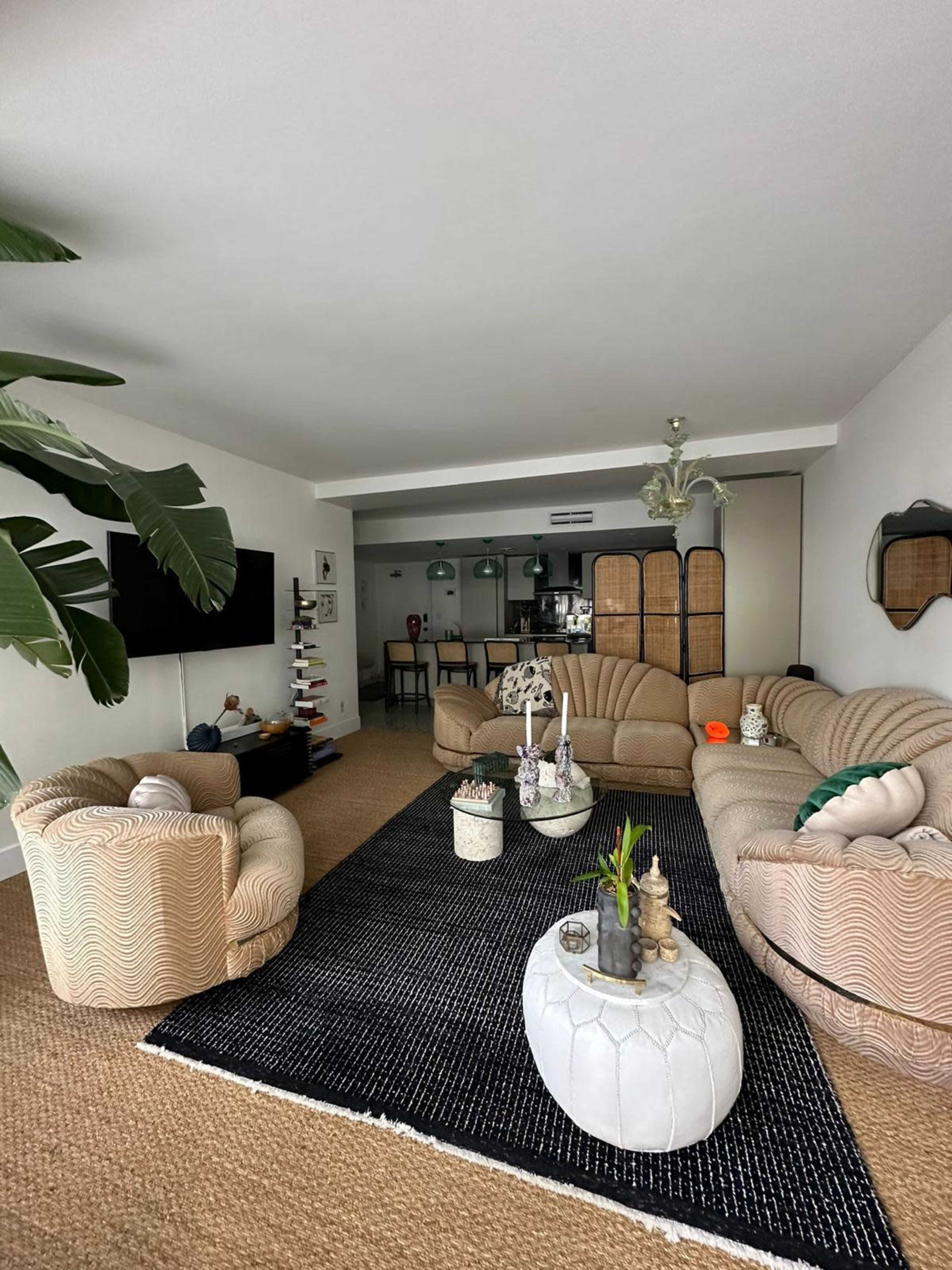 A modern living room featuring two curved sofas, a black area rug, a coffee table, and a dining area in the background.