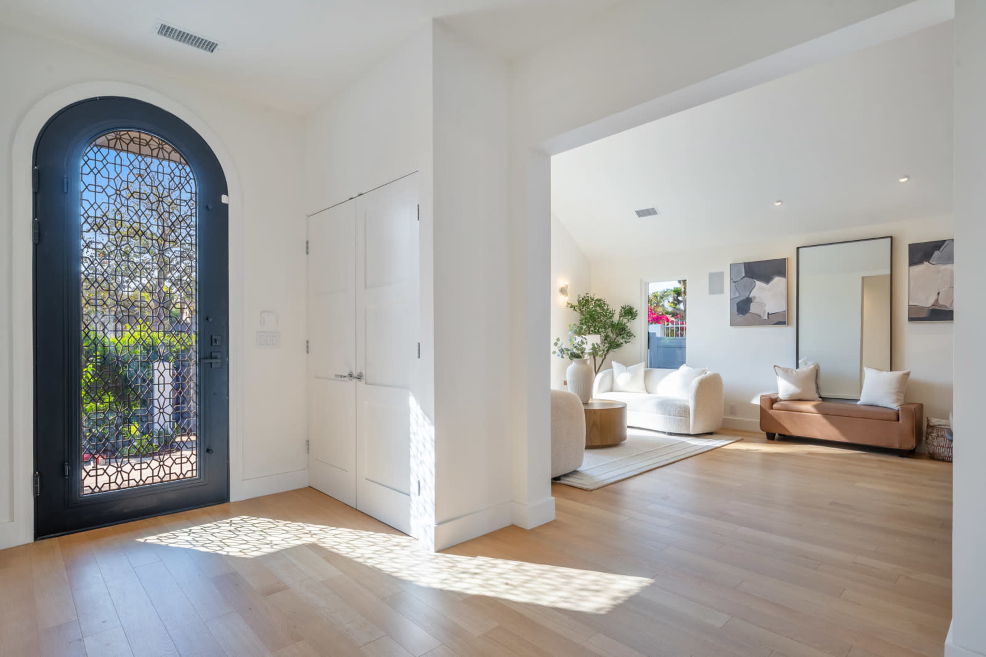 The image shows a bright interior entrance with a decorative door leading into a spacious living area featuring a sofa and artwork on the walls.