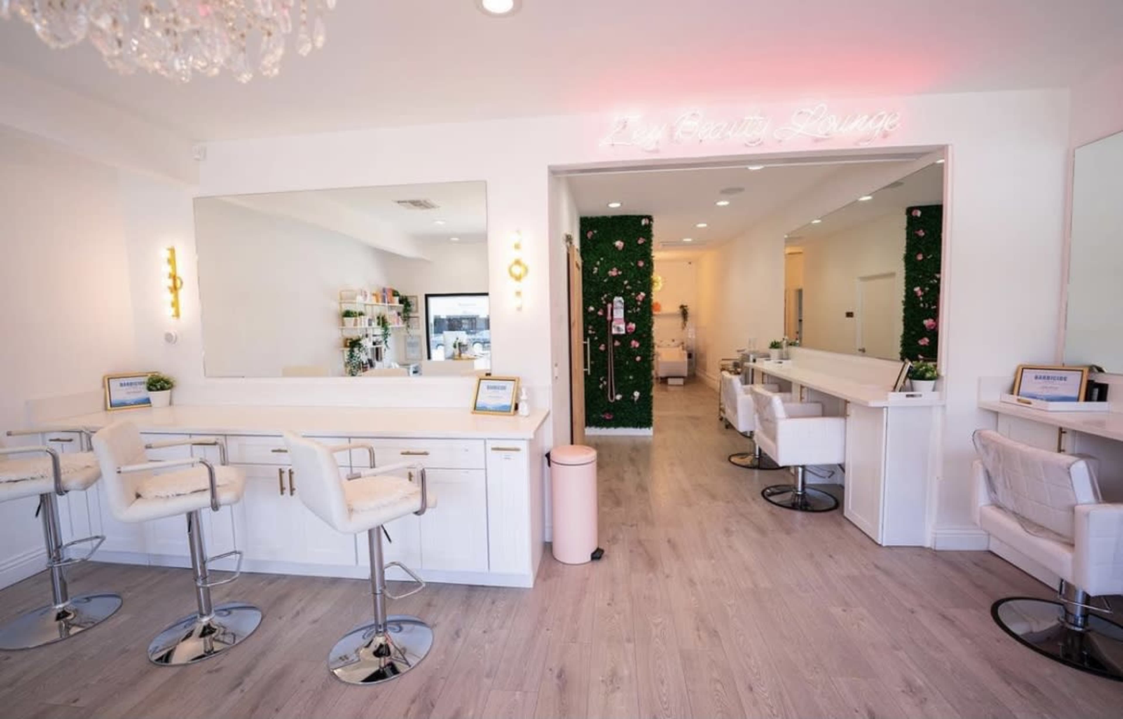 A modern beauty salon with white countertops, barstools, and a green wall featuring plants.