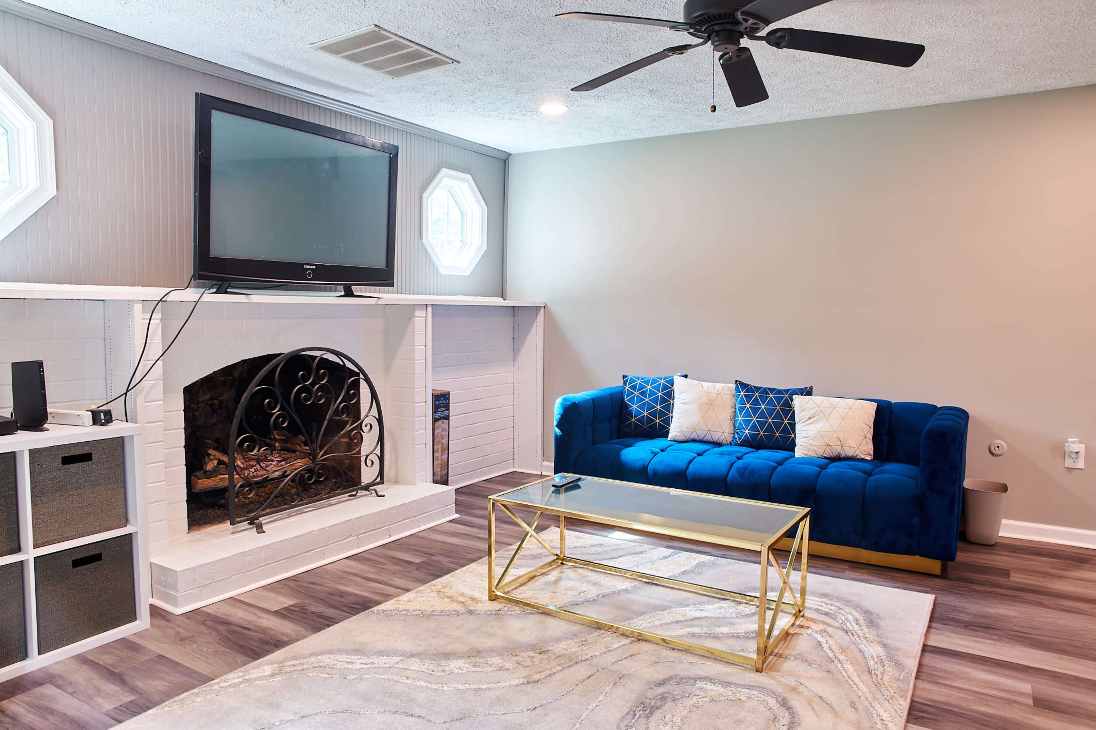 A modern living room featuring a blue sofa, a glass coffee table, a fireplace with decorative metalwork, and a mounted television.