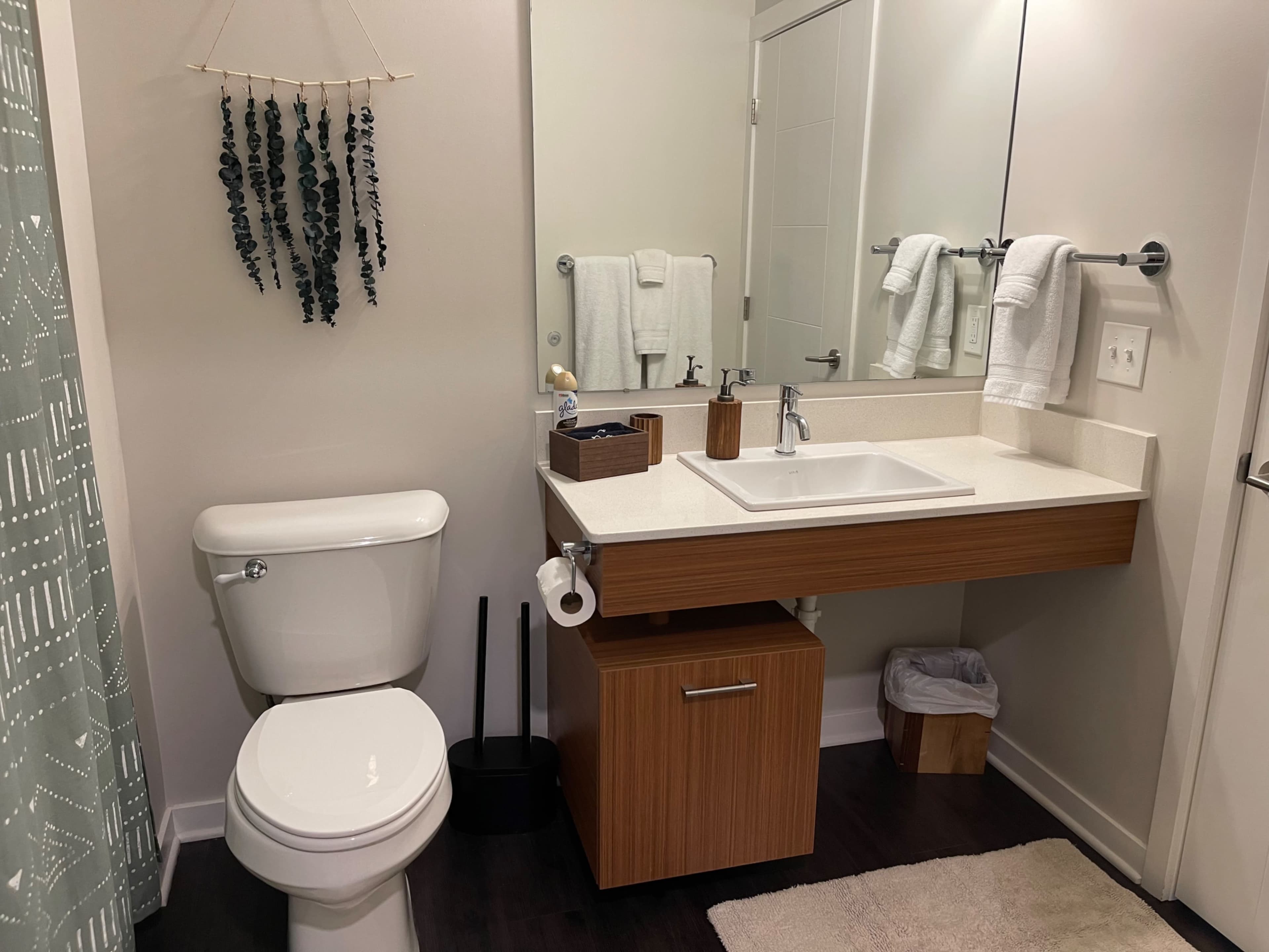 A modern bathroom featuring a white toilet, a wood vanity with a sink, and neatly arranged towels on a mirror cabinet.