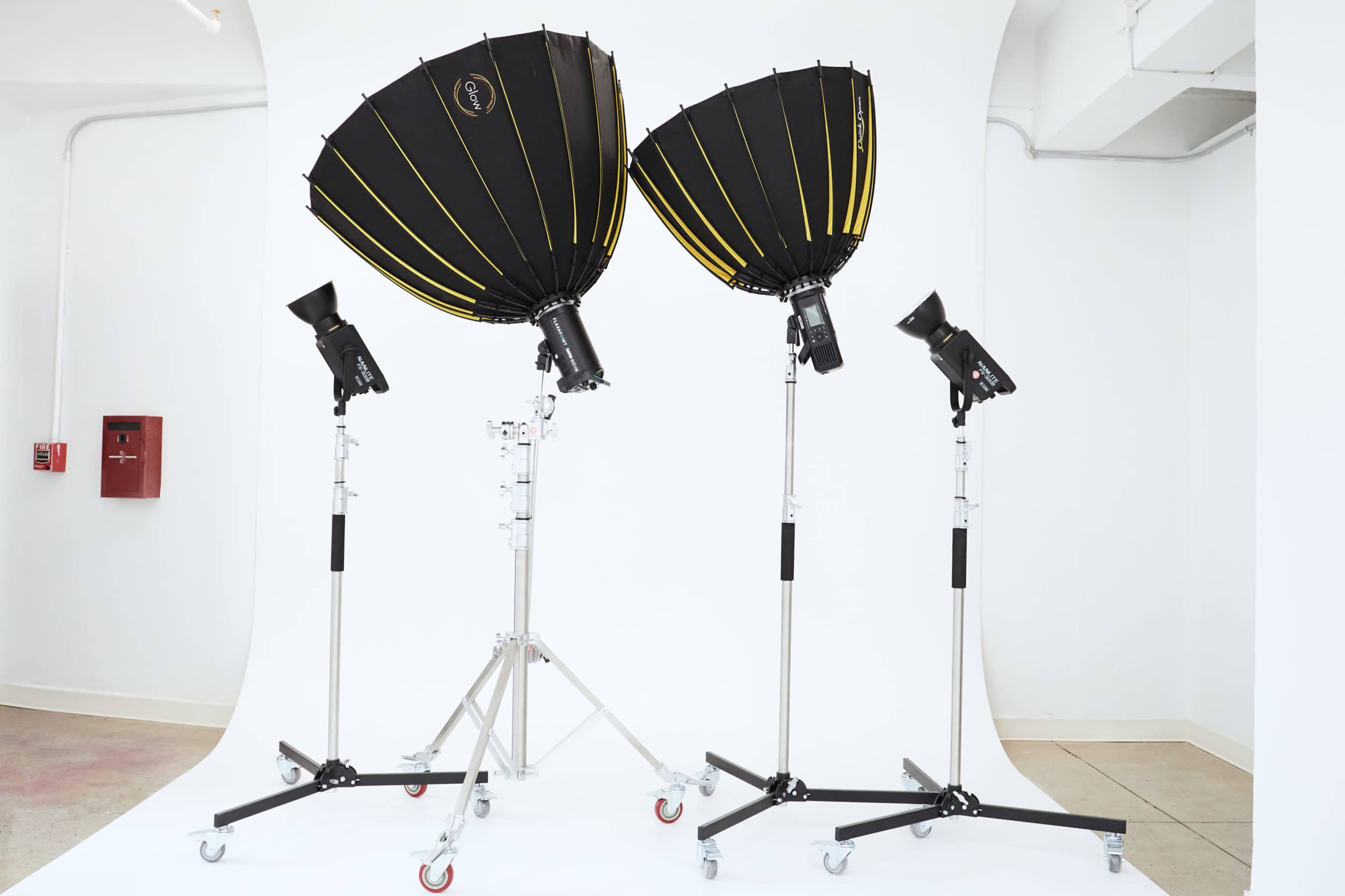 The image shows three studio light setups with softboxes on tall stands positioned against a white backdrop.