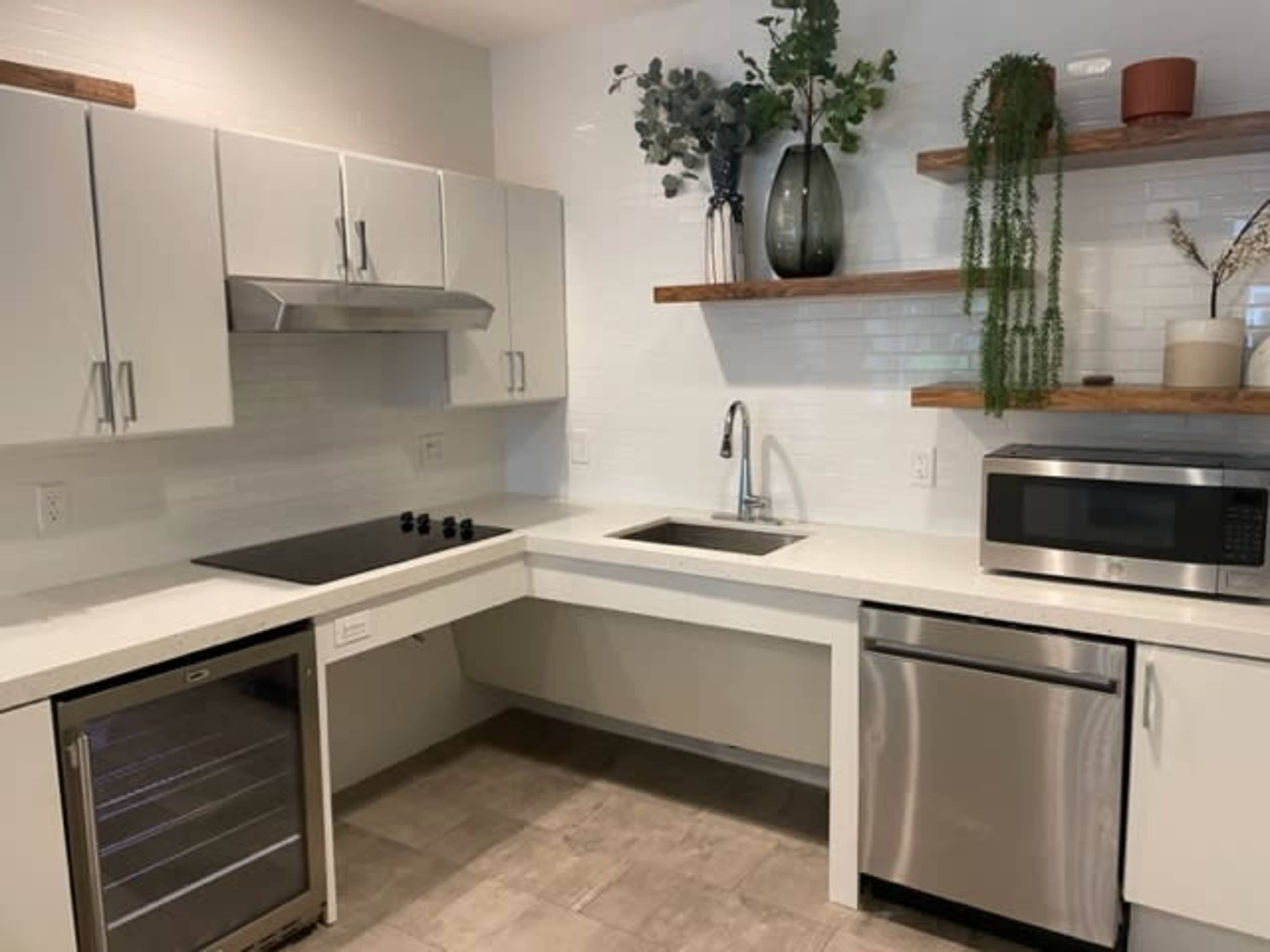 A modern kitchen with white cabinetry, a stainless steel sink and dishwasher, and wooden shelves displaying plants and decor.