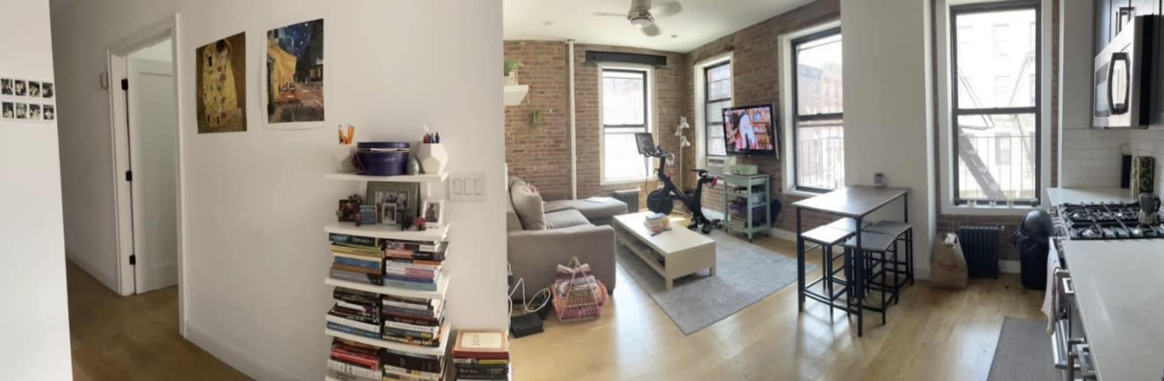 The image shows a spacious apartment interior with a hallway leading to a living area that features large windows, a sitting area, and a kitchen.