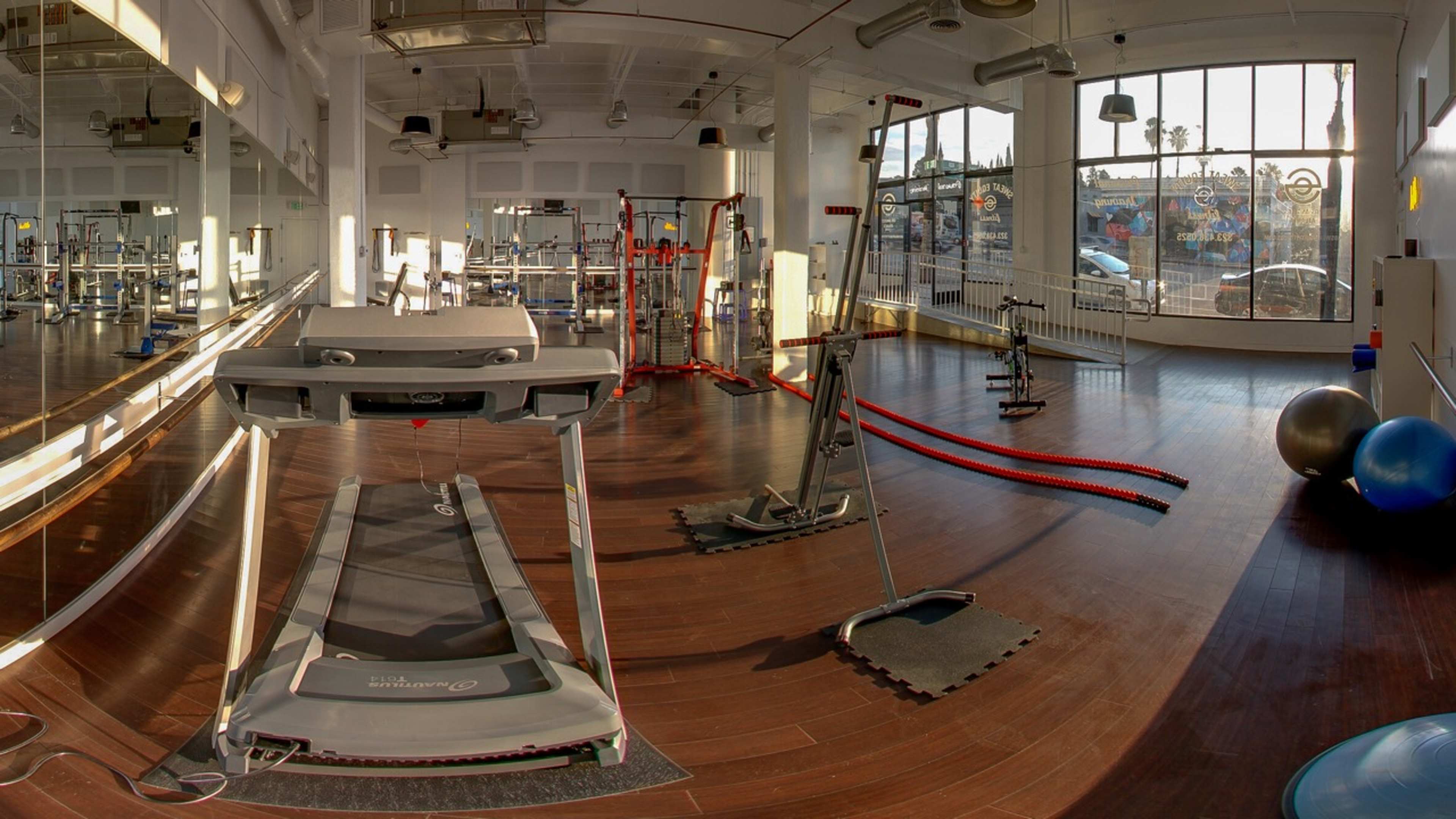 A modern gym interior featuring a treadmill, exercise equipment, and large windows allowing natural light to fill the space.