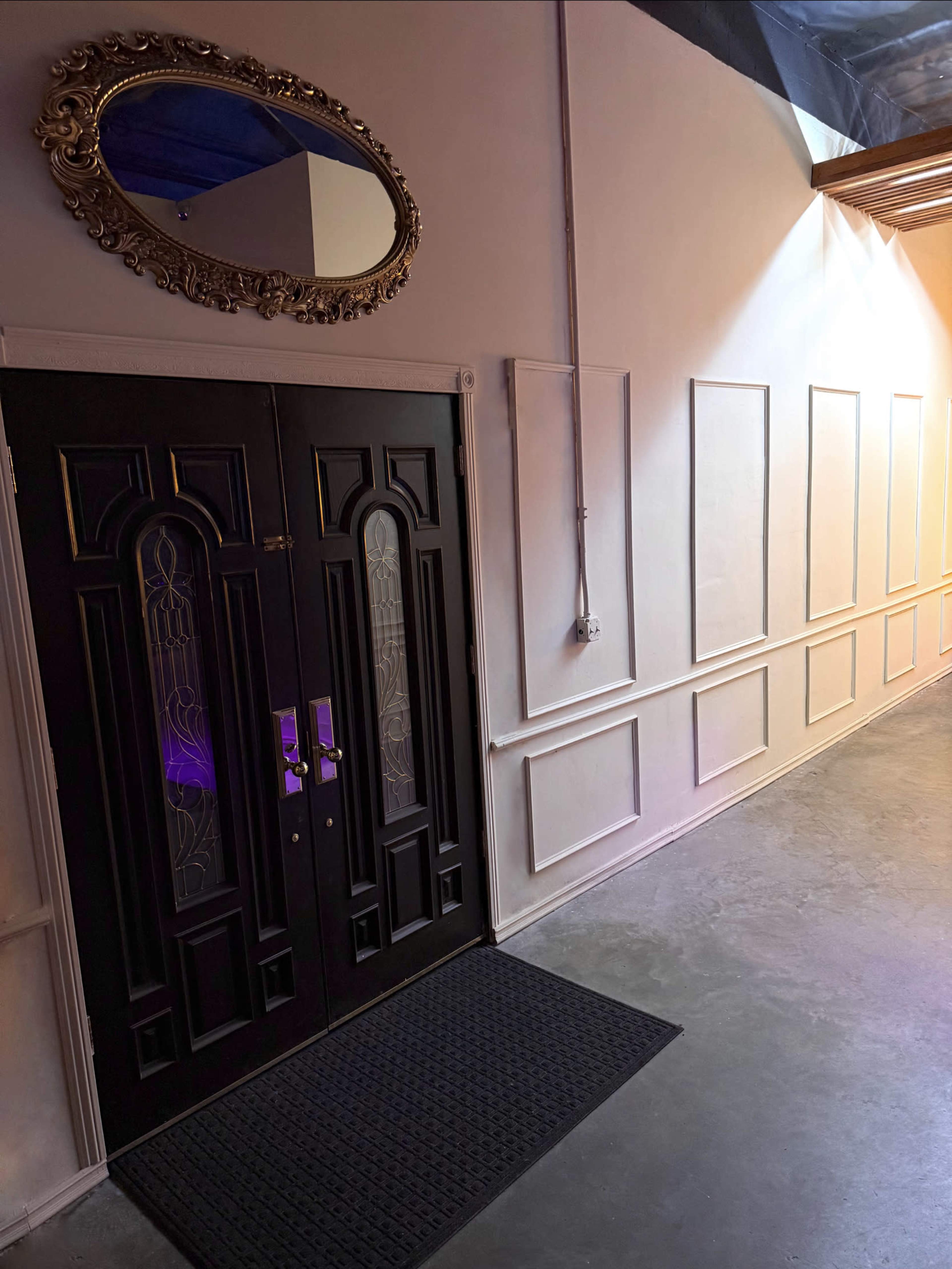 The image shows a set of elegant double doors with decorative glass inserts, positioned against a wall featuring moldings, with a mirror hanging above the doors.