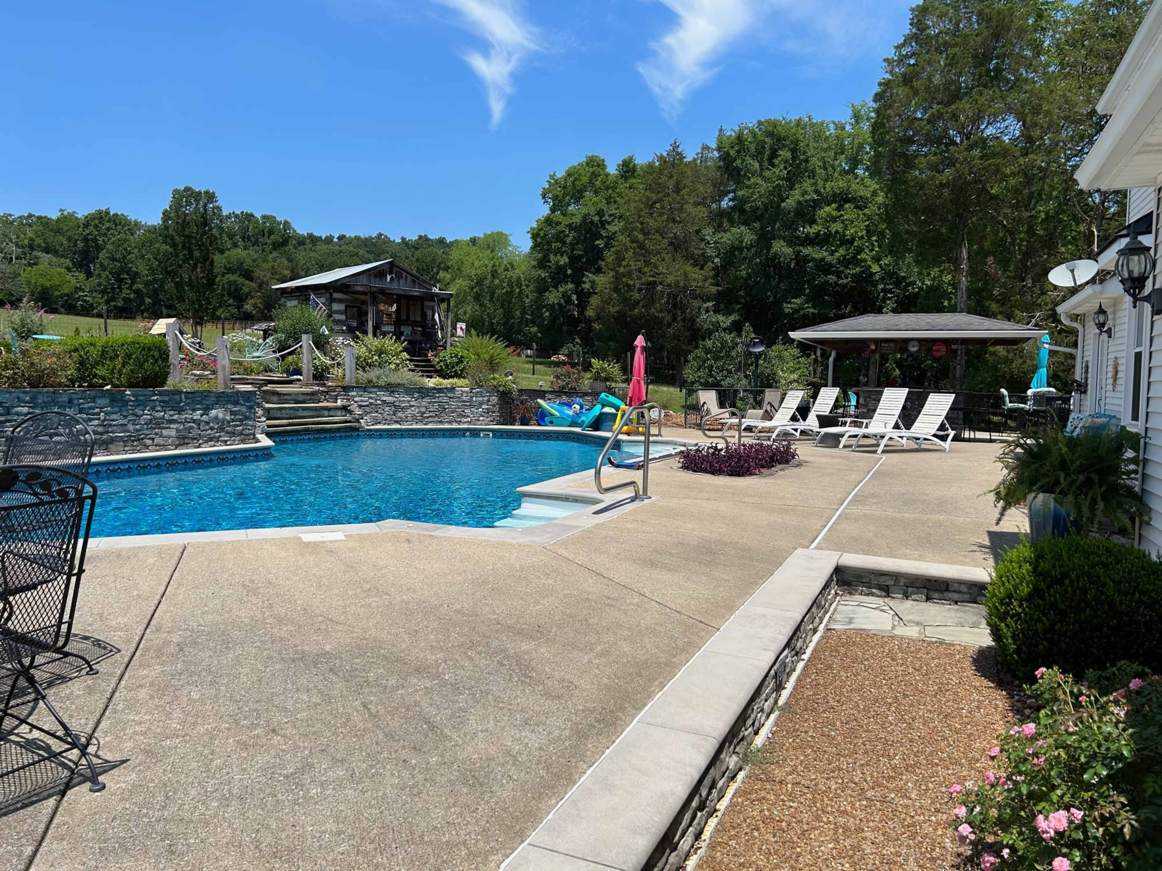 The image shows a residential backyard with a swimming pool, lounge chairs, and a gazebo surrounded by greenery.