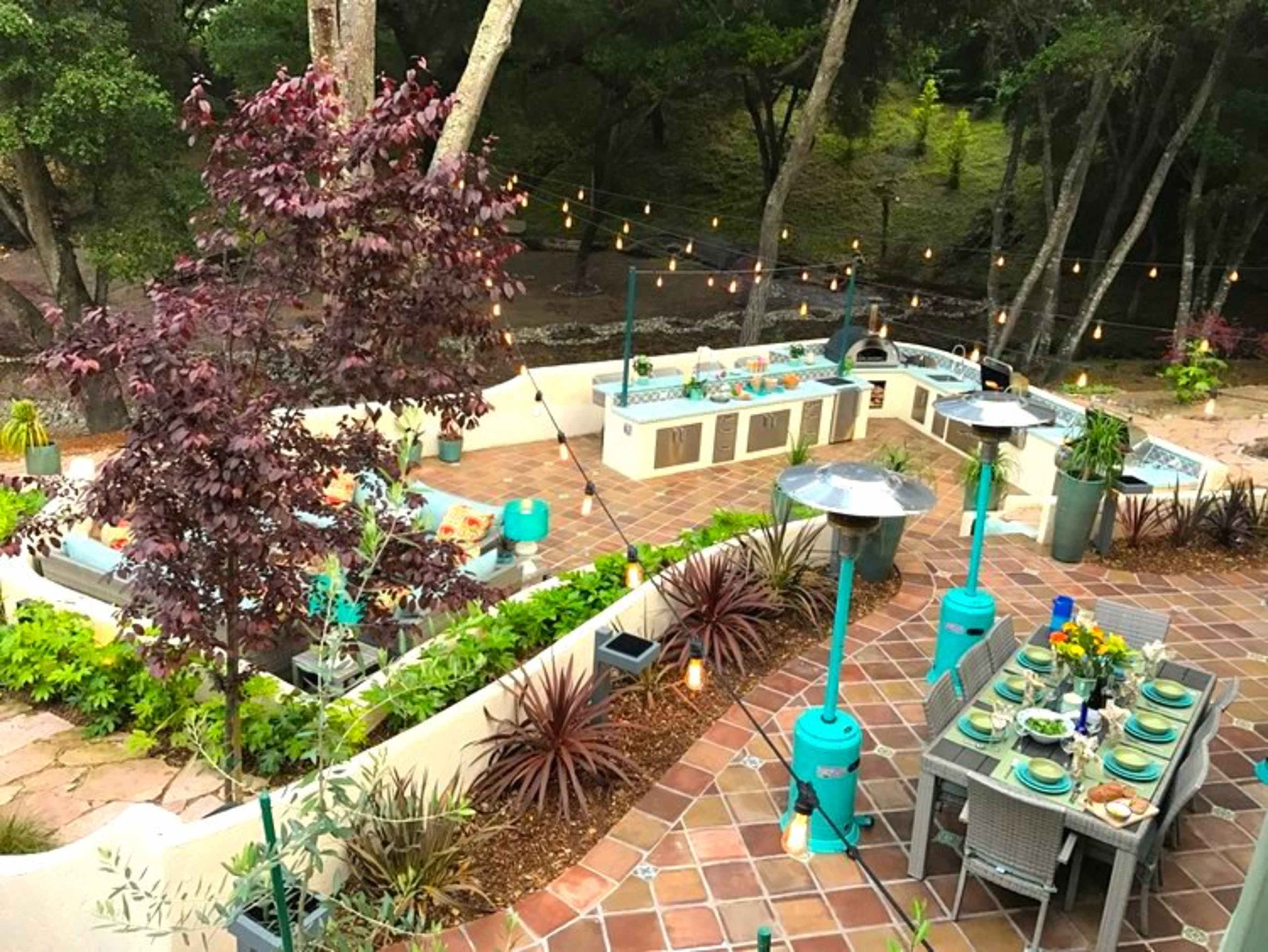 An outdoor kitchen and dining area decorated with string lights, surrounded by trees and various plants.