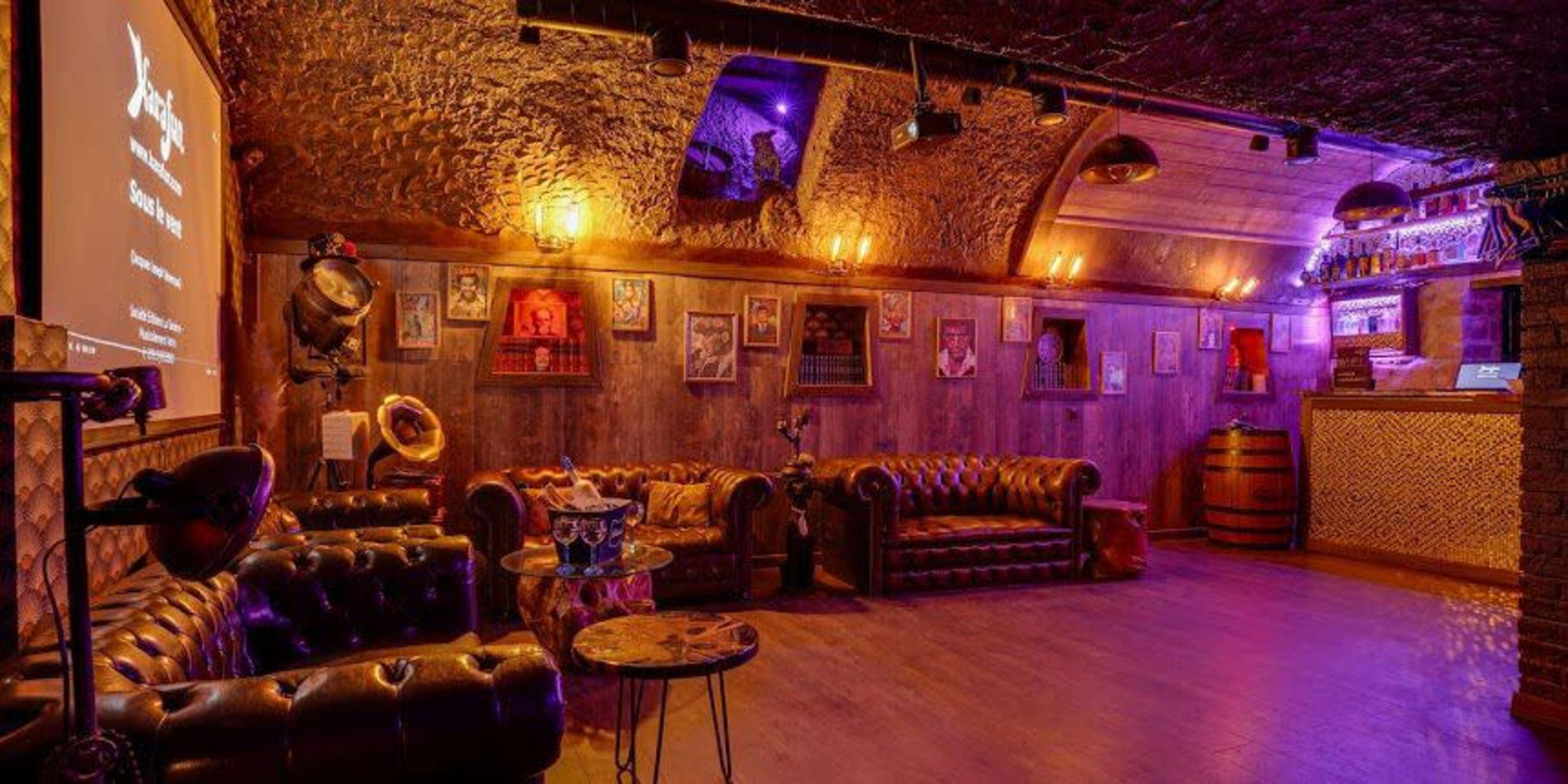 The image depicts a warmly lit lounge area featuring leather couches, wooden walls adorned with artwork, and a bar in the background.