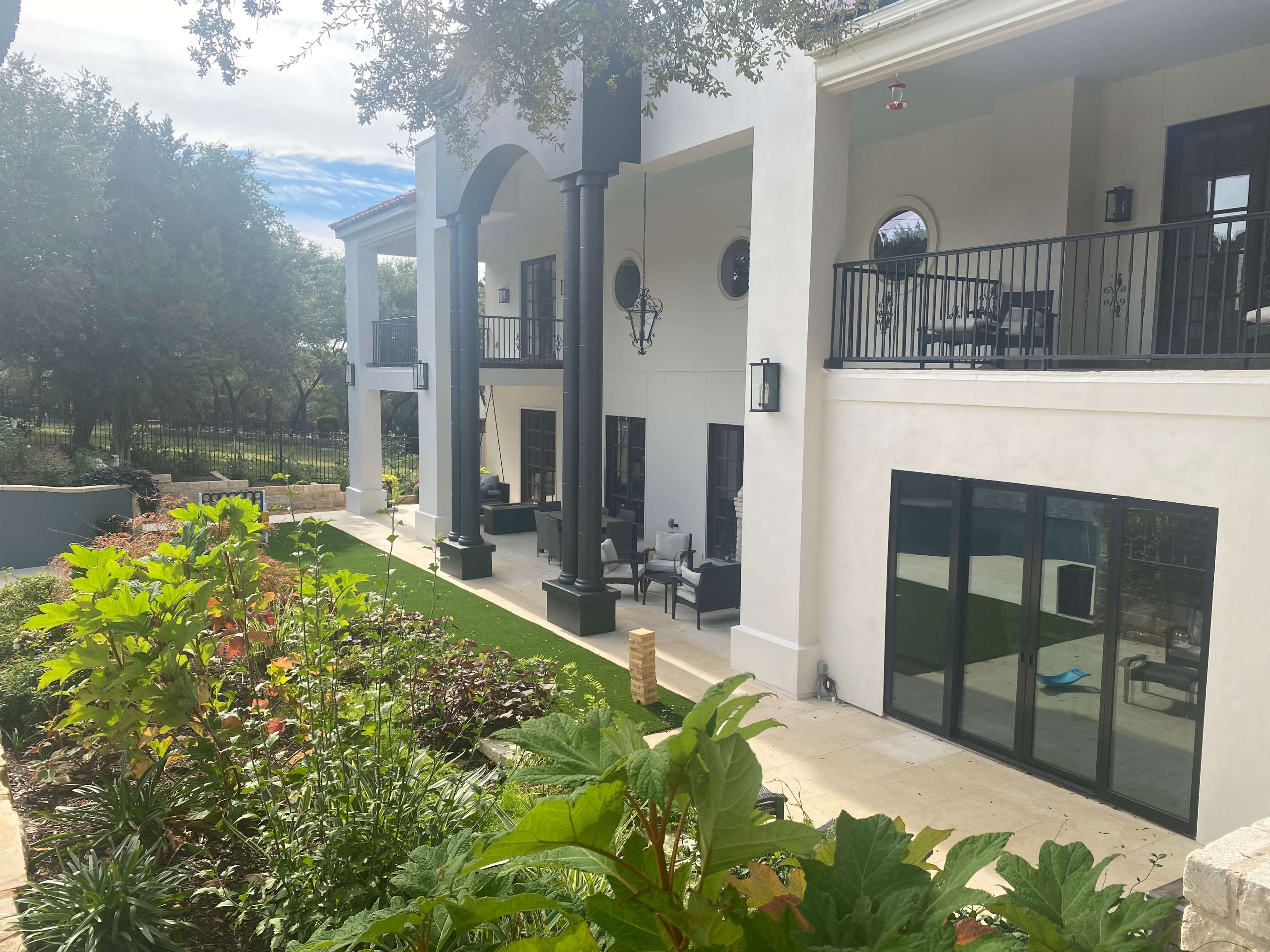The image shows a two-story modern building with a landscaped garden, featuring a covered patio and large windows.