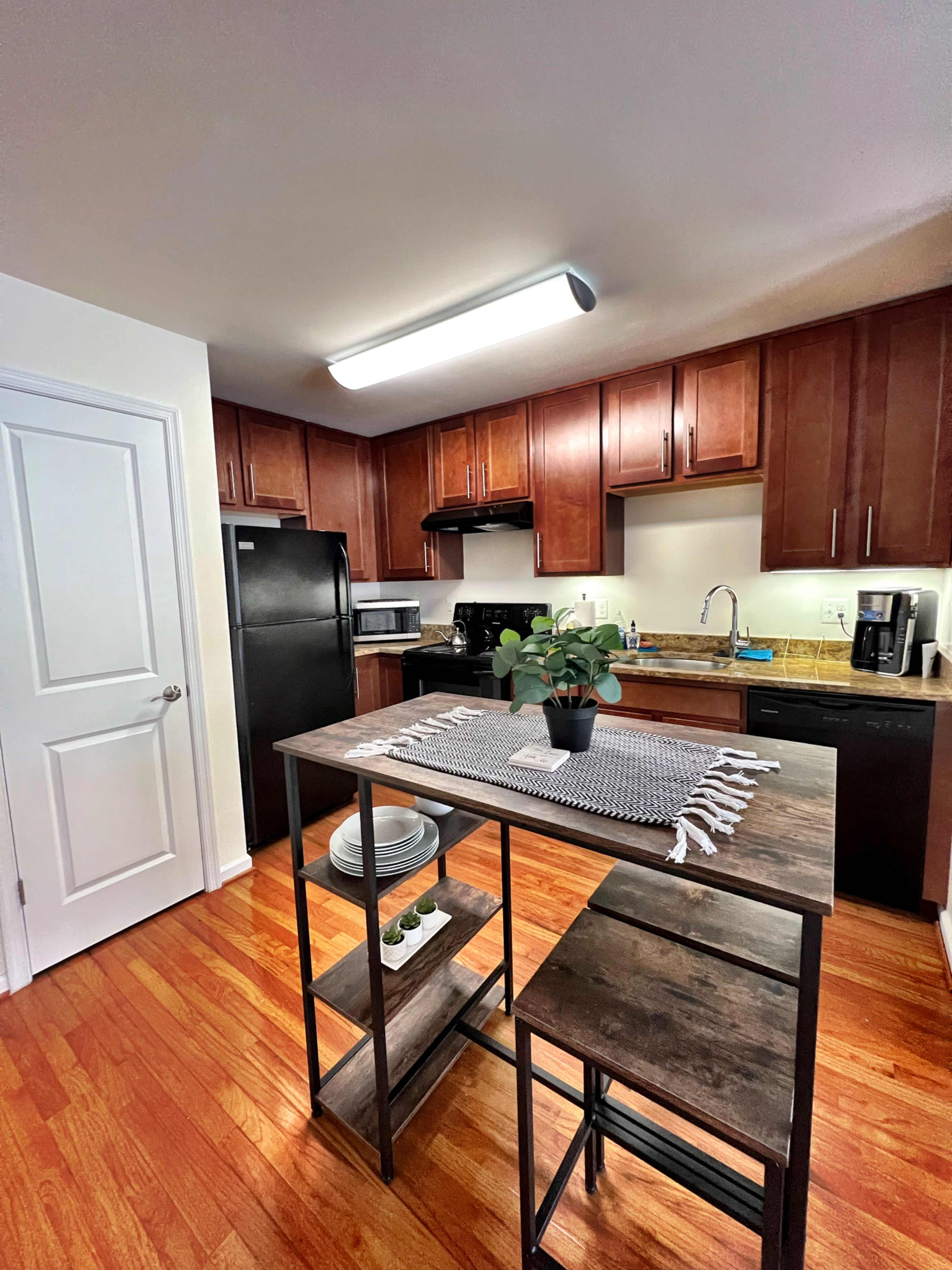 The image shows a modern kitchen featuring dark wood cabinetry, a black refrigerator, and a small dining table with two stools.