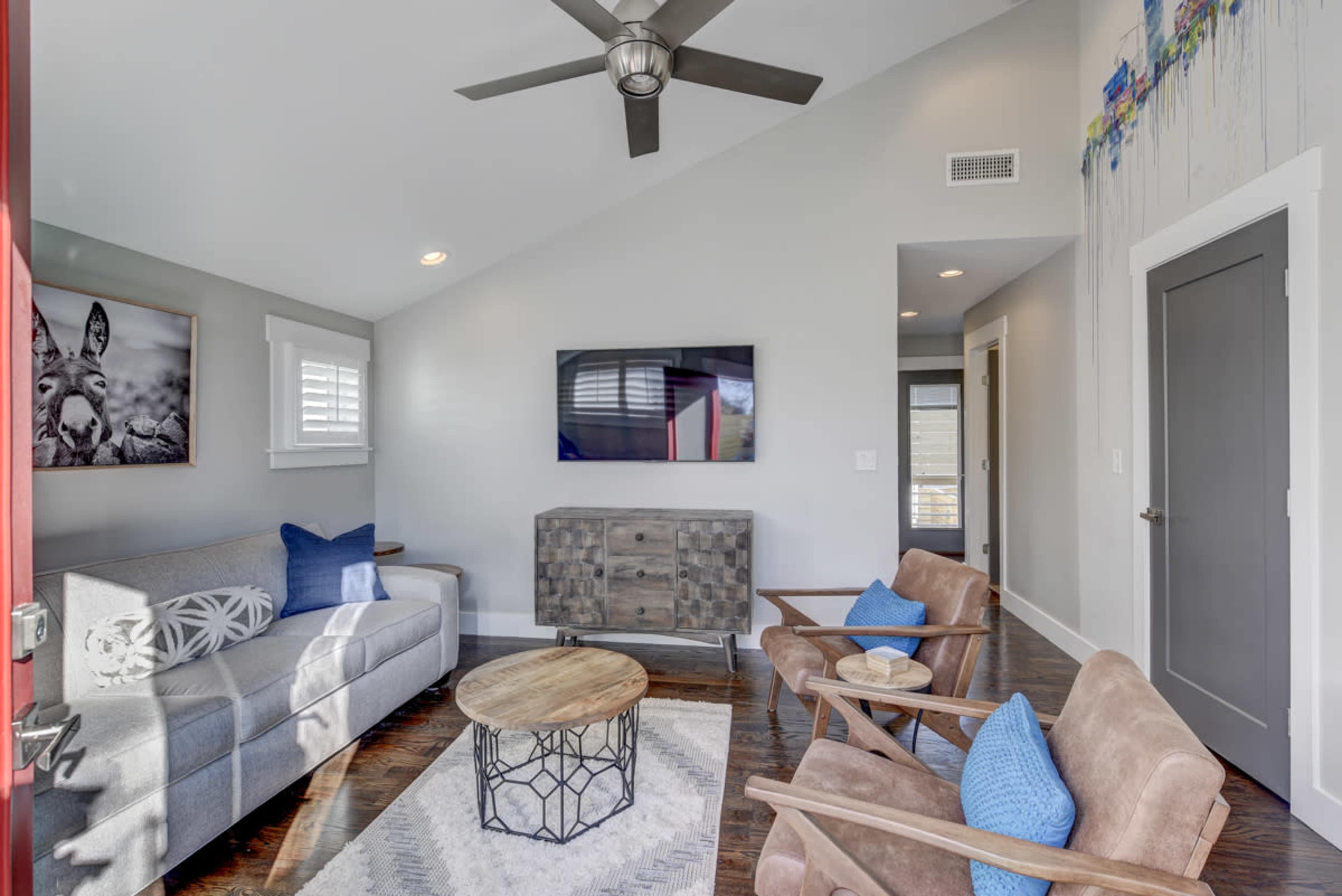 A modern living room with a gray sofa, two brown armchairs, a round wooden coffee table, and a wall-mounted television.
