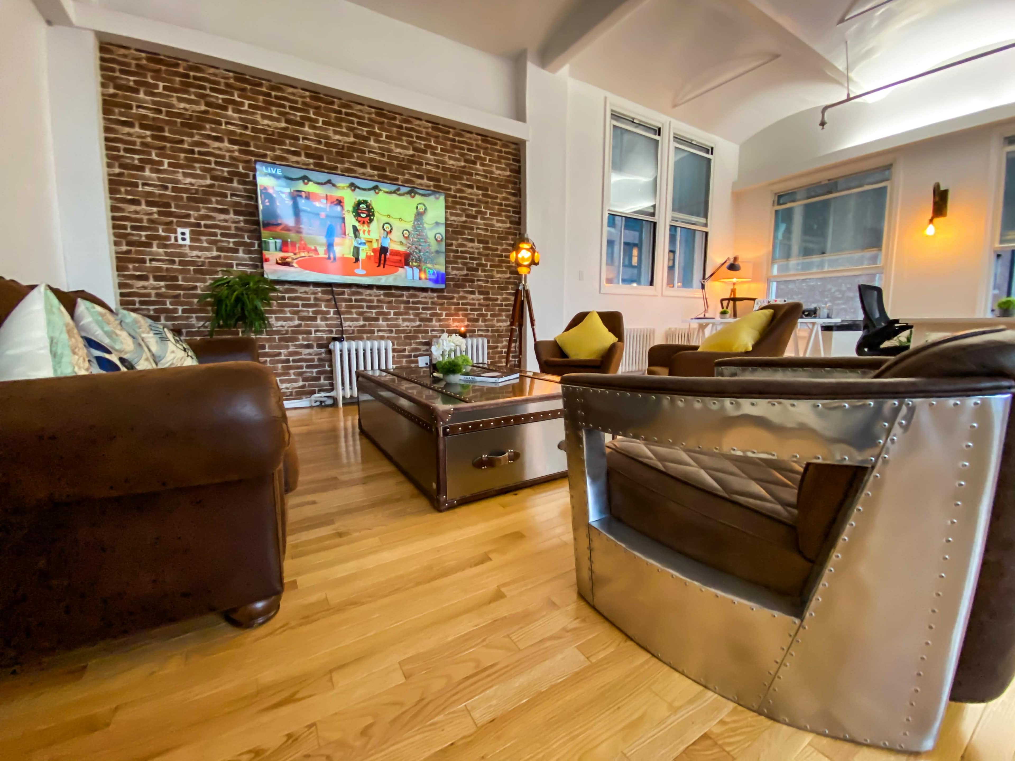 A modern living room featuring a brown leather sofa, a decorative coffee table, and a flat-screen TV mounted on a brick accent wall.