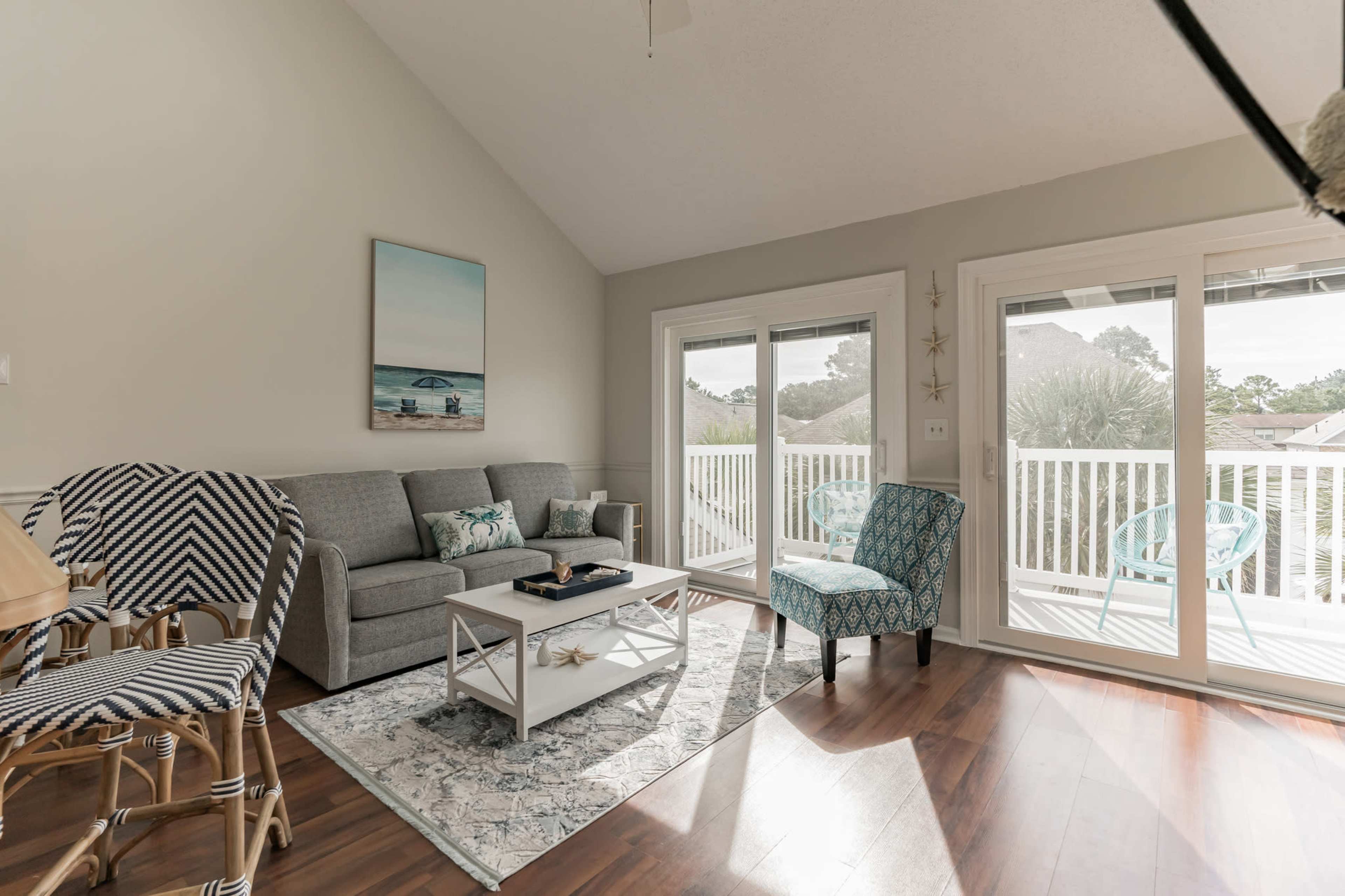 A living room with a gray sofa, a light blue accent chair, a white coffee table on an area rug, and large sliding glass doors leading to a balcony.