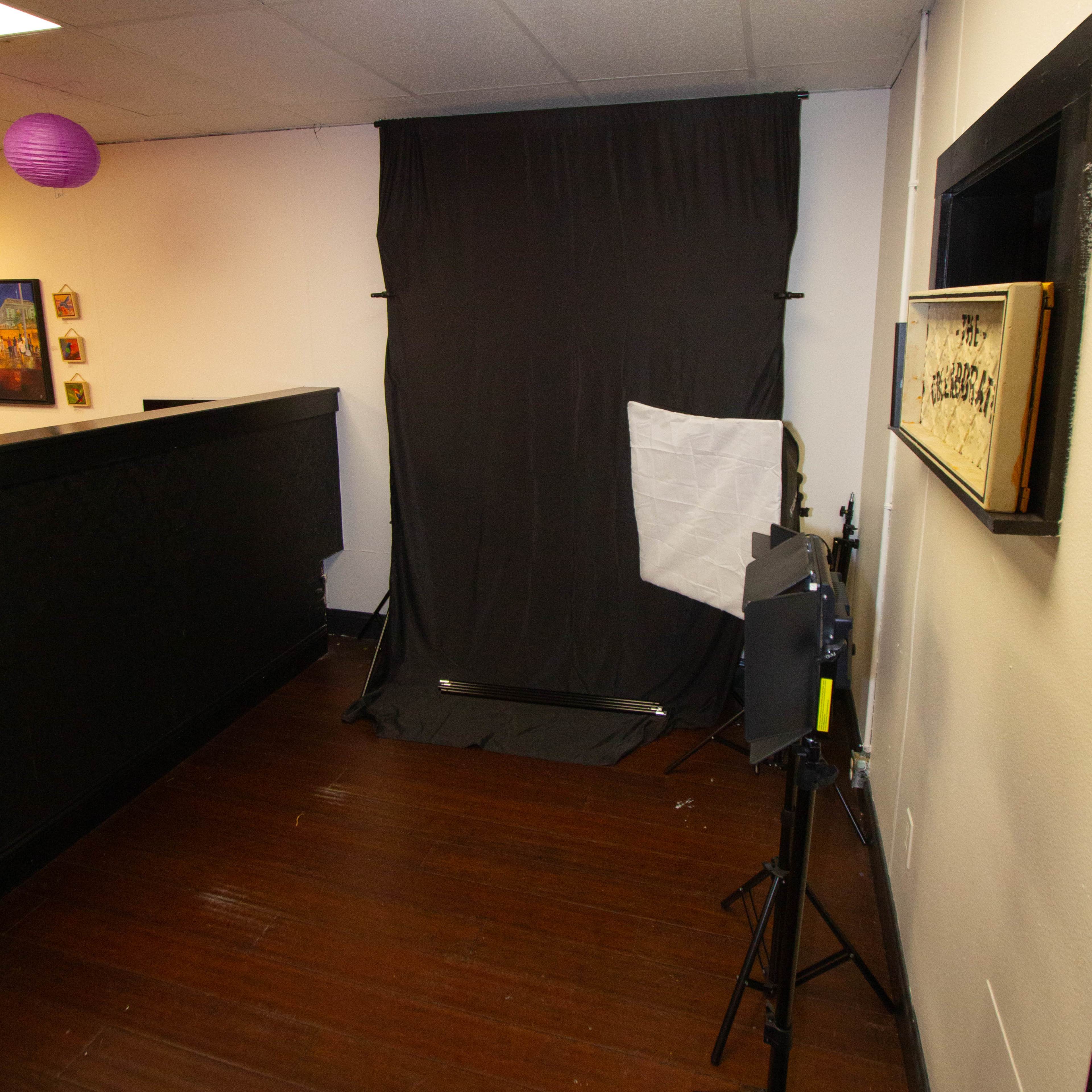The image shows a photography setup in a room featuring a black backdrop, a light source, and a reception desk.