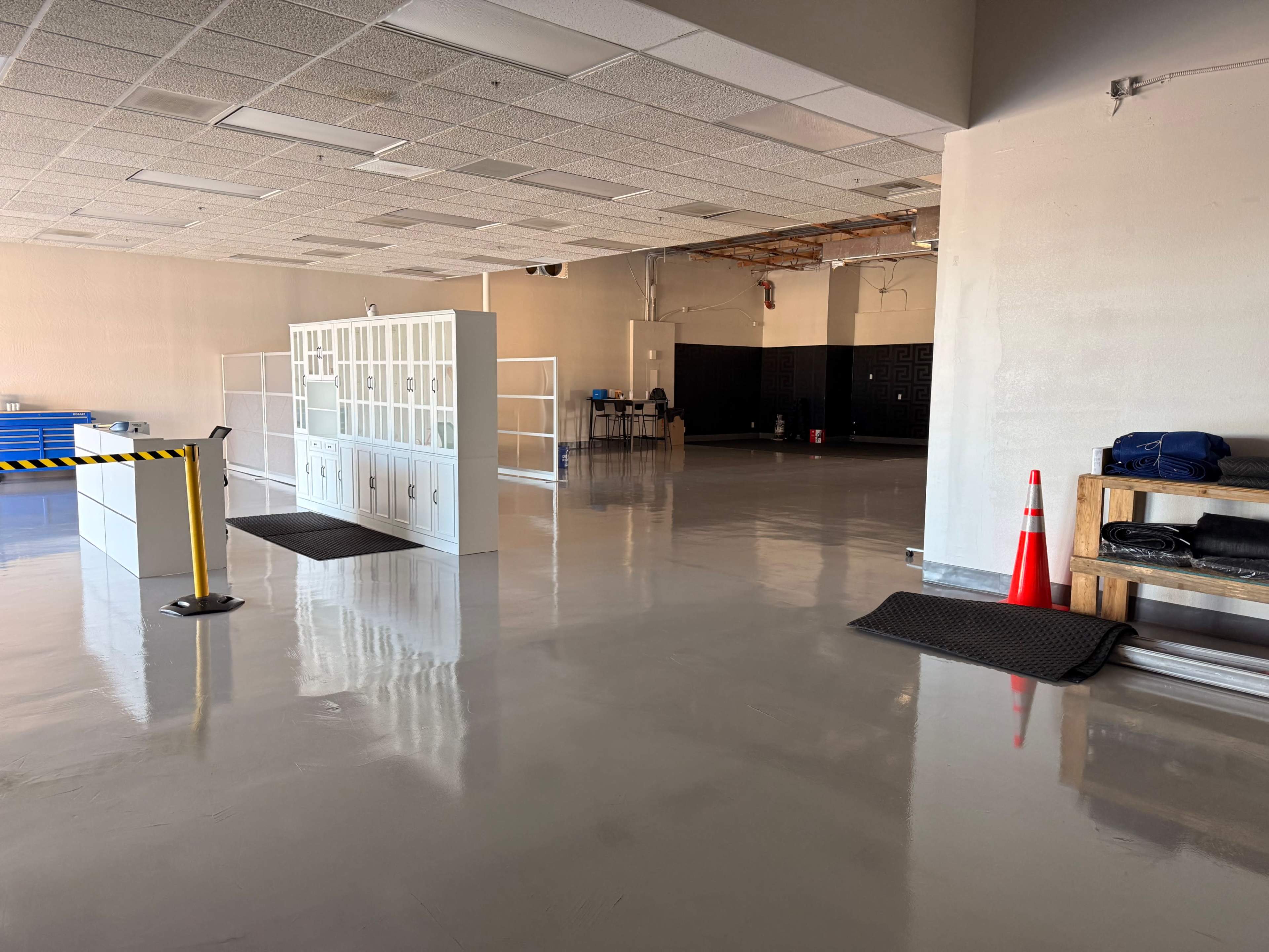 The image shows a spacious, empty room with a polished concrete floor, featuring a white locker unit on the left and a partitioned area in the background.