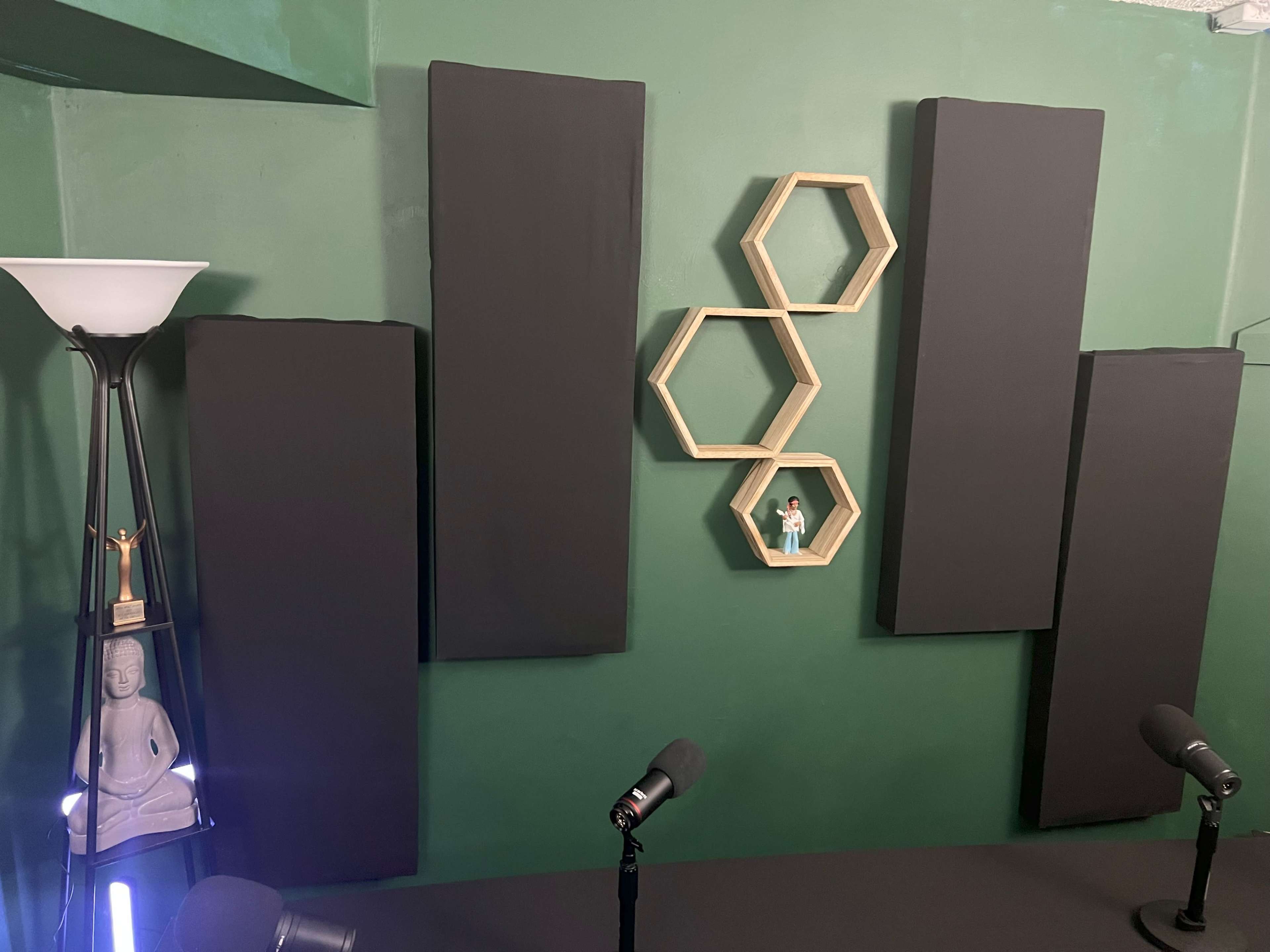 A green room with black sound panels on the walls, a lamp, a statue, and a hexagonal shelf holding a small figure.