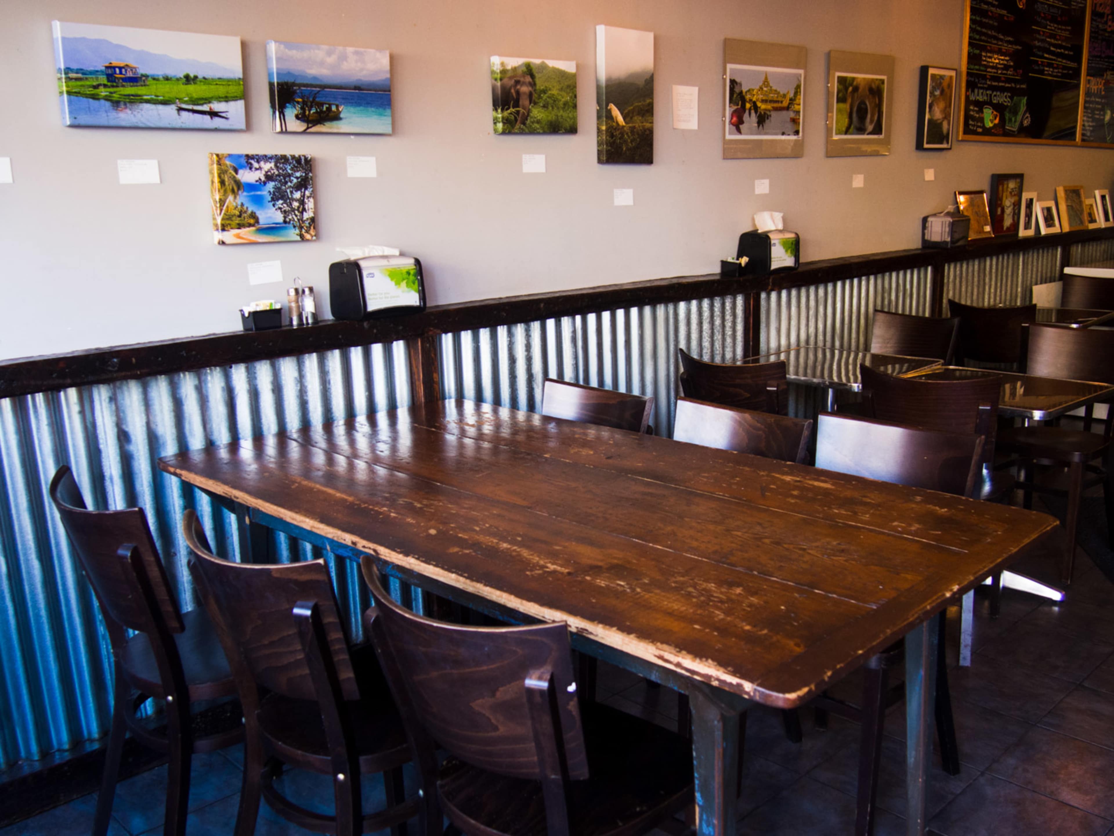A wooden table surrounded by dark chairs is set against a wall adorned with framed photographs in a casual dining space.