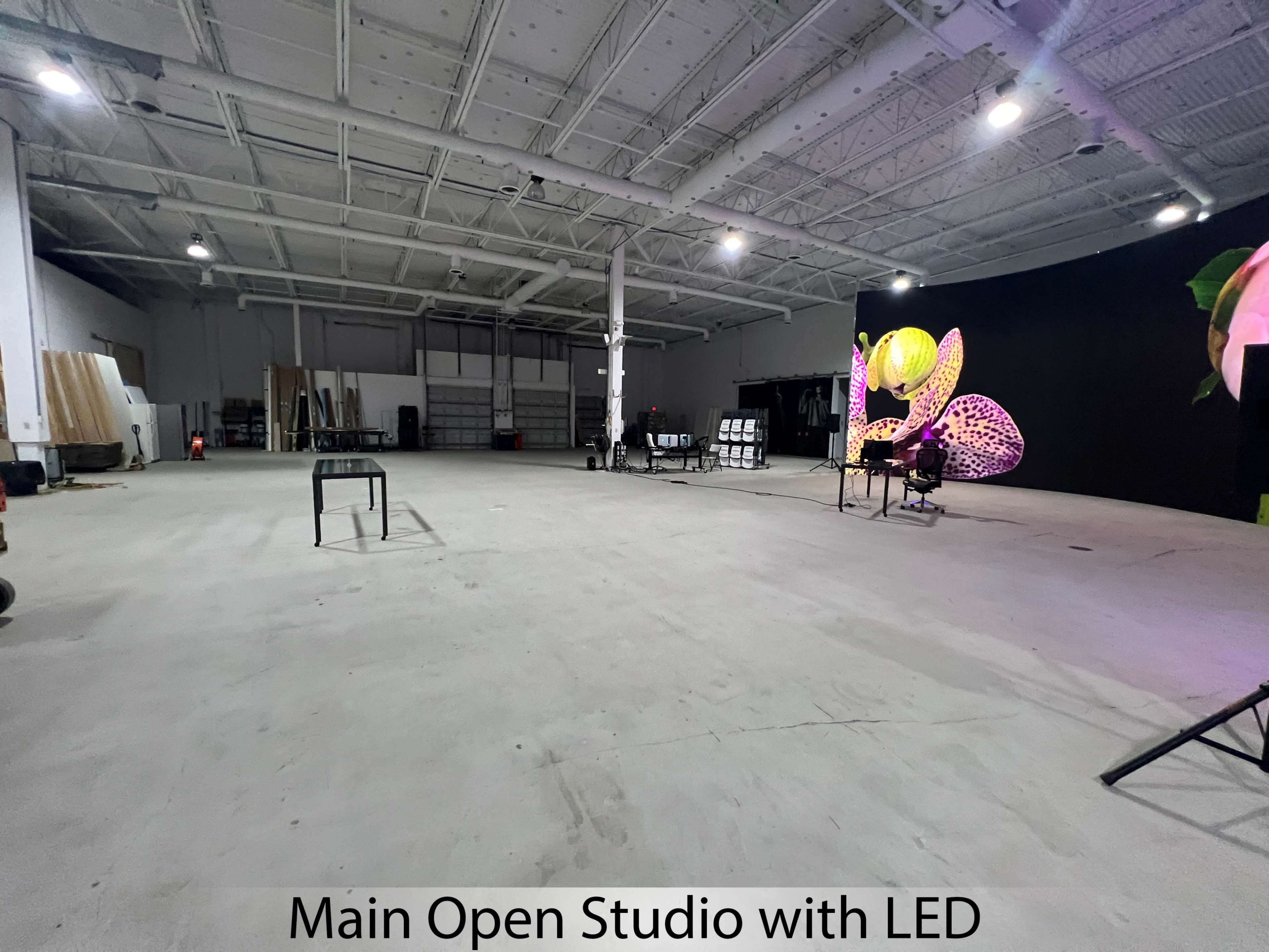 The image shows a spacious open studio area with a plain concrete floor, illuminated lighting, and a large LED screen featuring vibrant visuals on one wall.