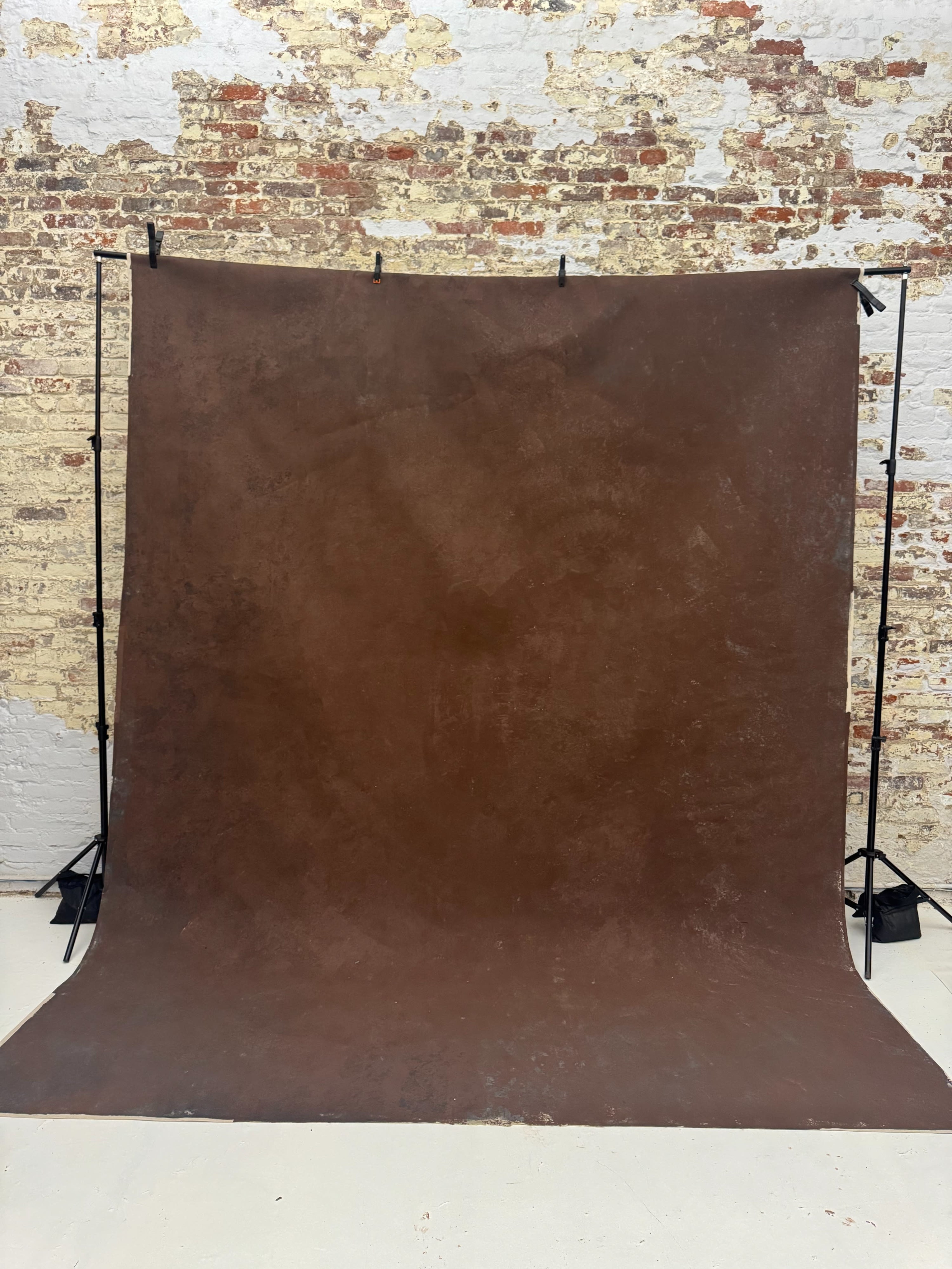 The image shows a brown backdrop draped on a support structure against a brick wall.