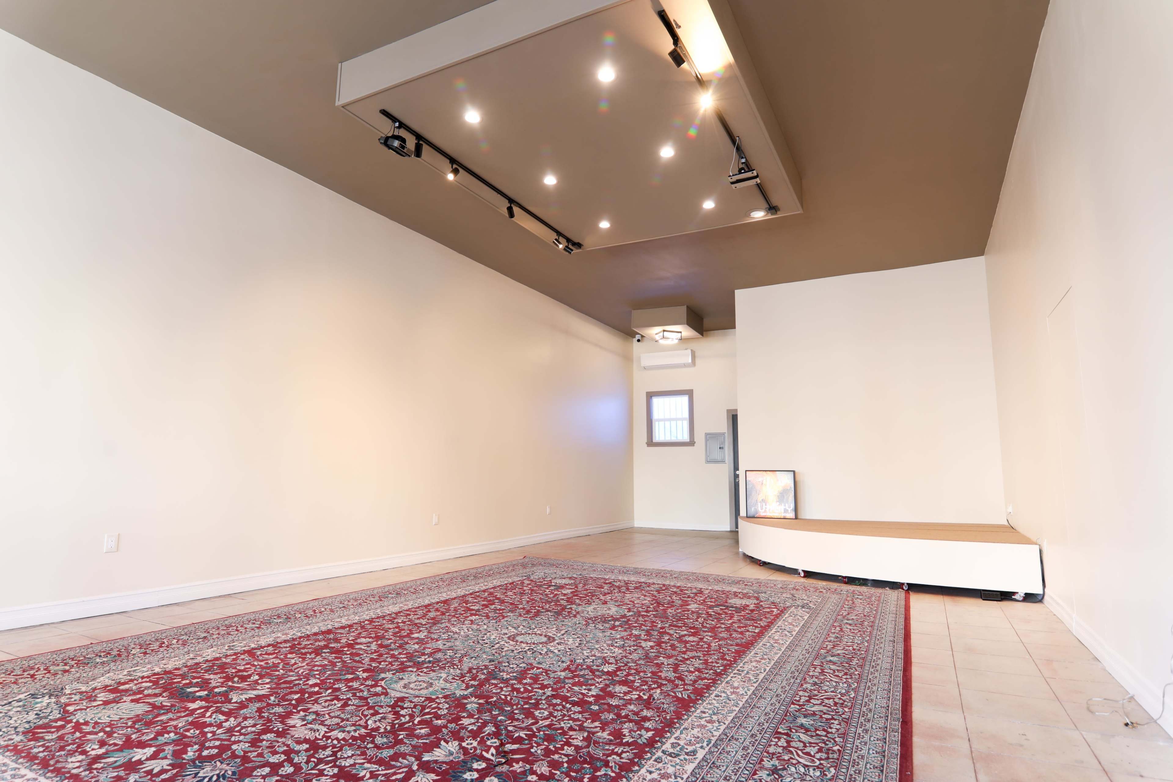 An empty room with a patterned rug, a wall-mounted display screen, and recessed lighting.