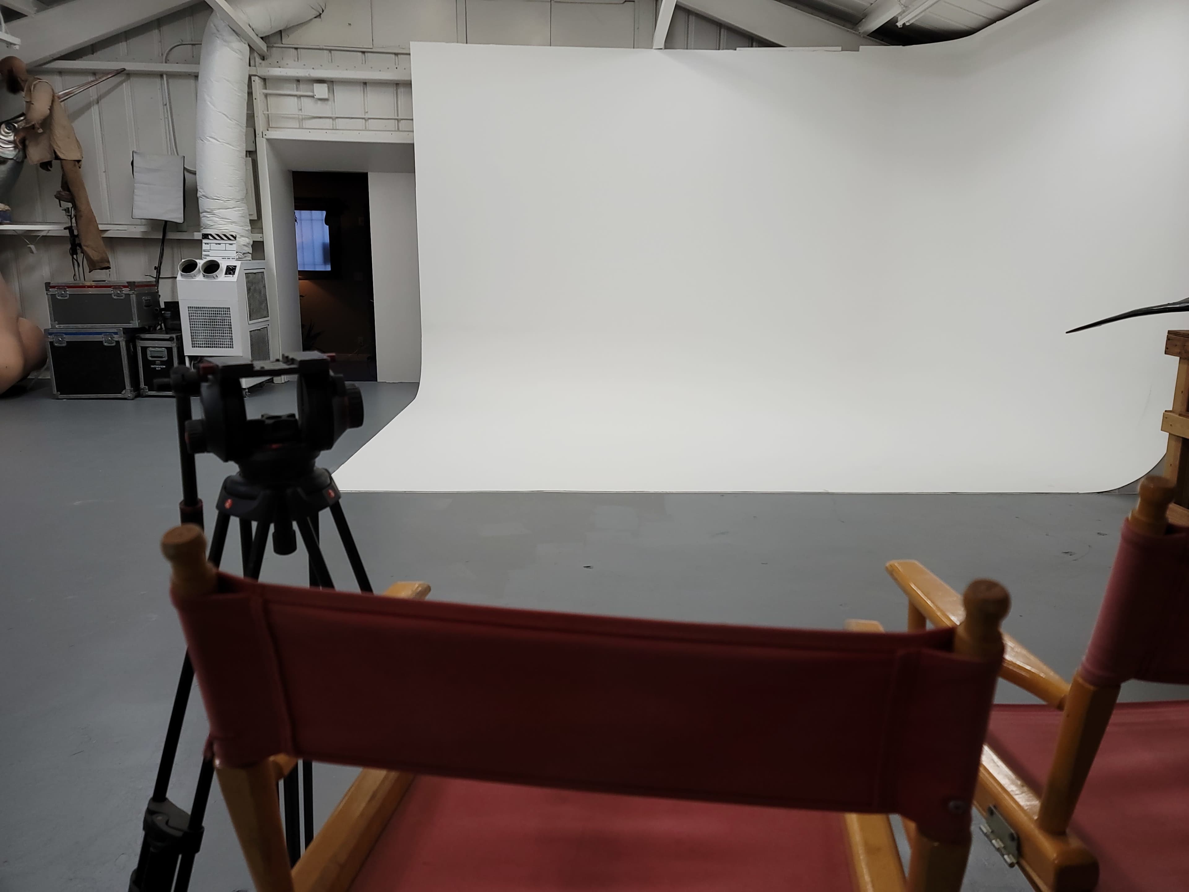 A photography studio features a white backdrop, a tripod-mounted camera, and two red director's chairs facing the scene.