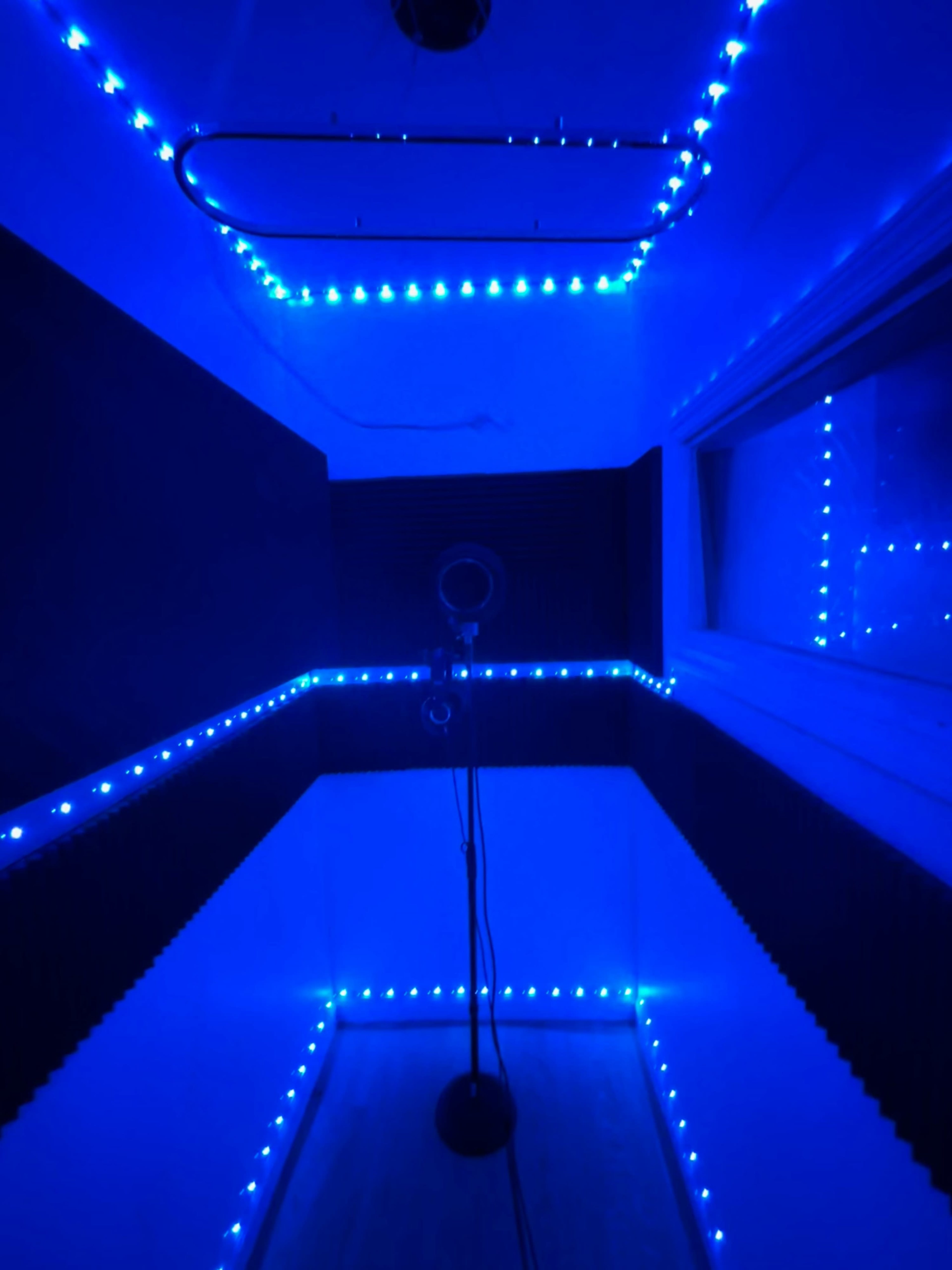 The image shows a sound booth illuminated with blue LED lights and equipped with a microphone on a stand.