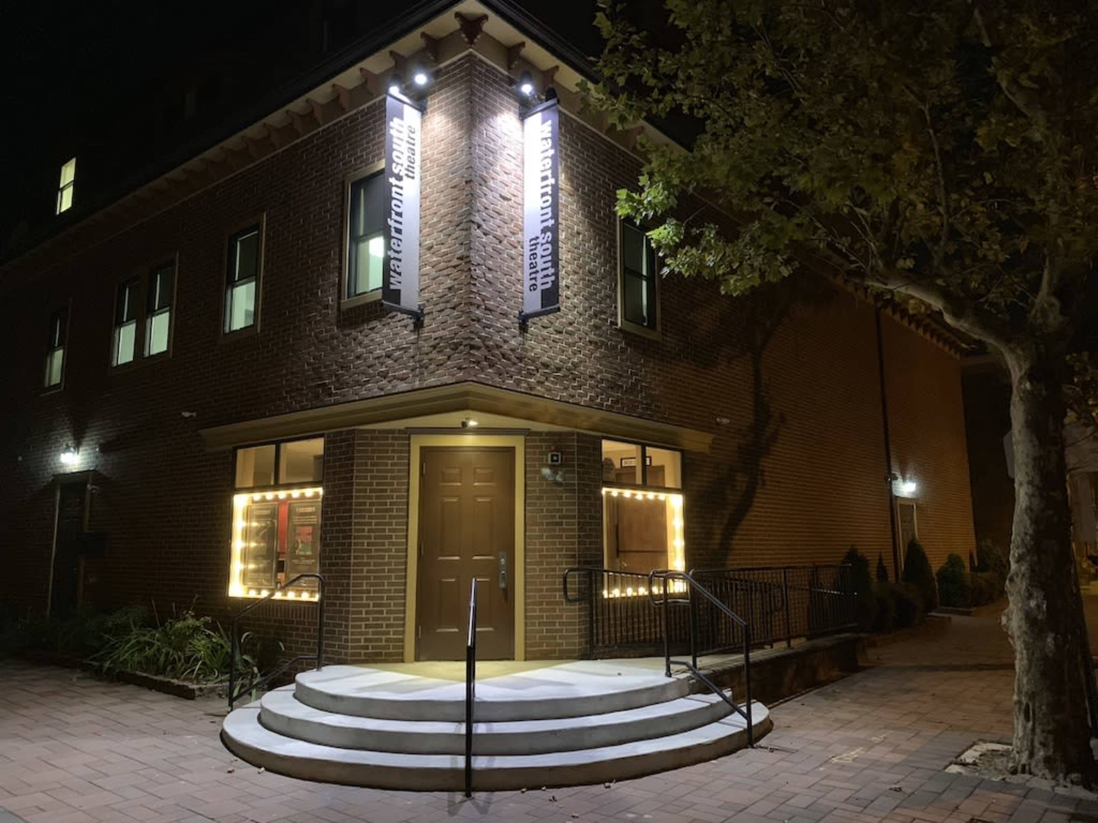 A brick building with illuminated signage and a staircase leading to a double-door entrance, flanked by bright mirrors.