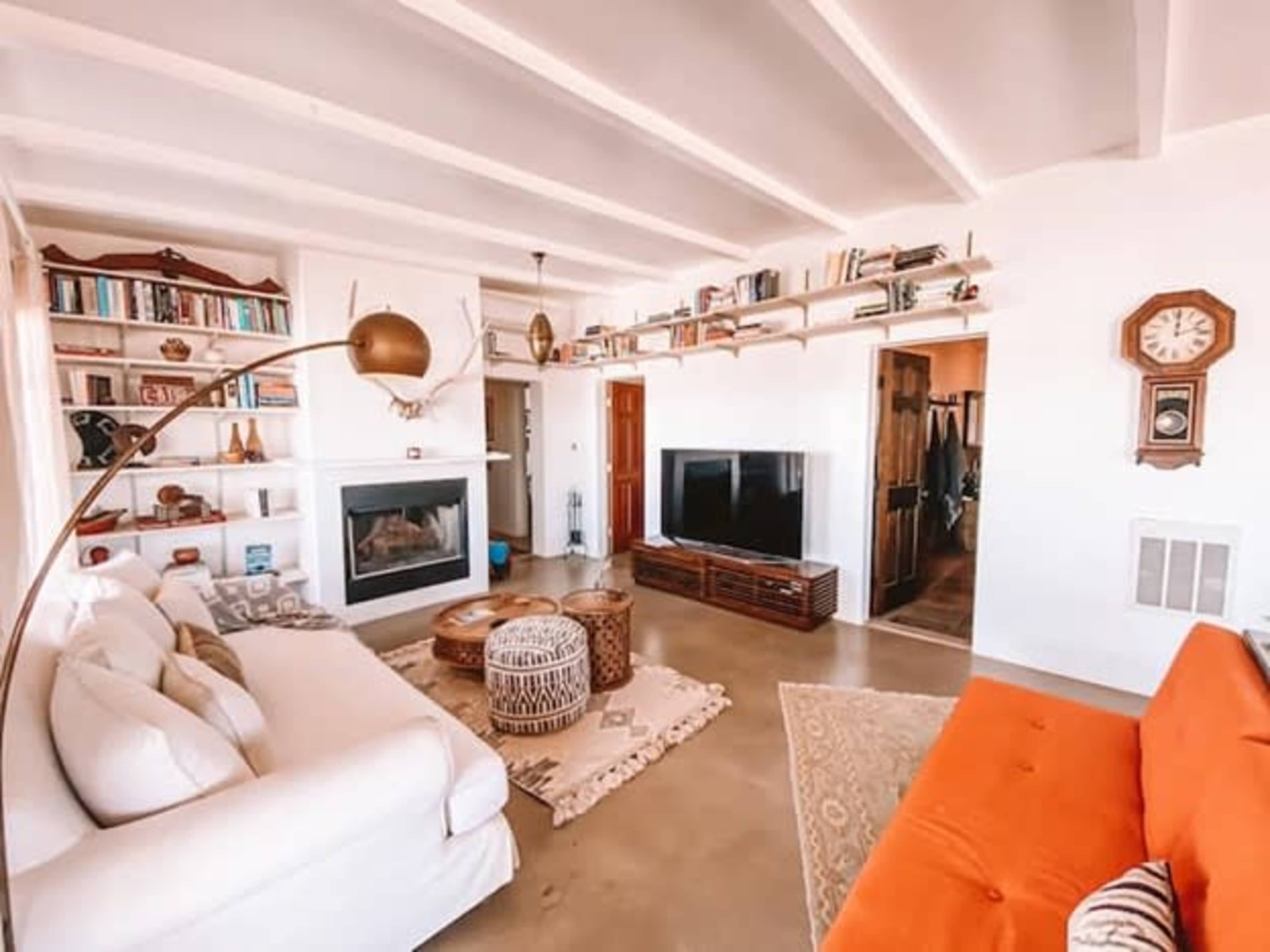The living room features a white sectional sofa, an orange couch, a large television, a fireplace, and bookshelves filled with books.