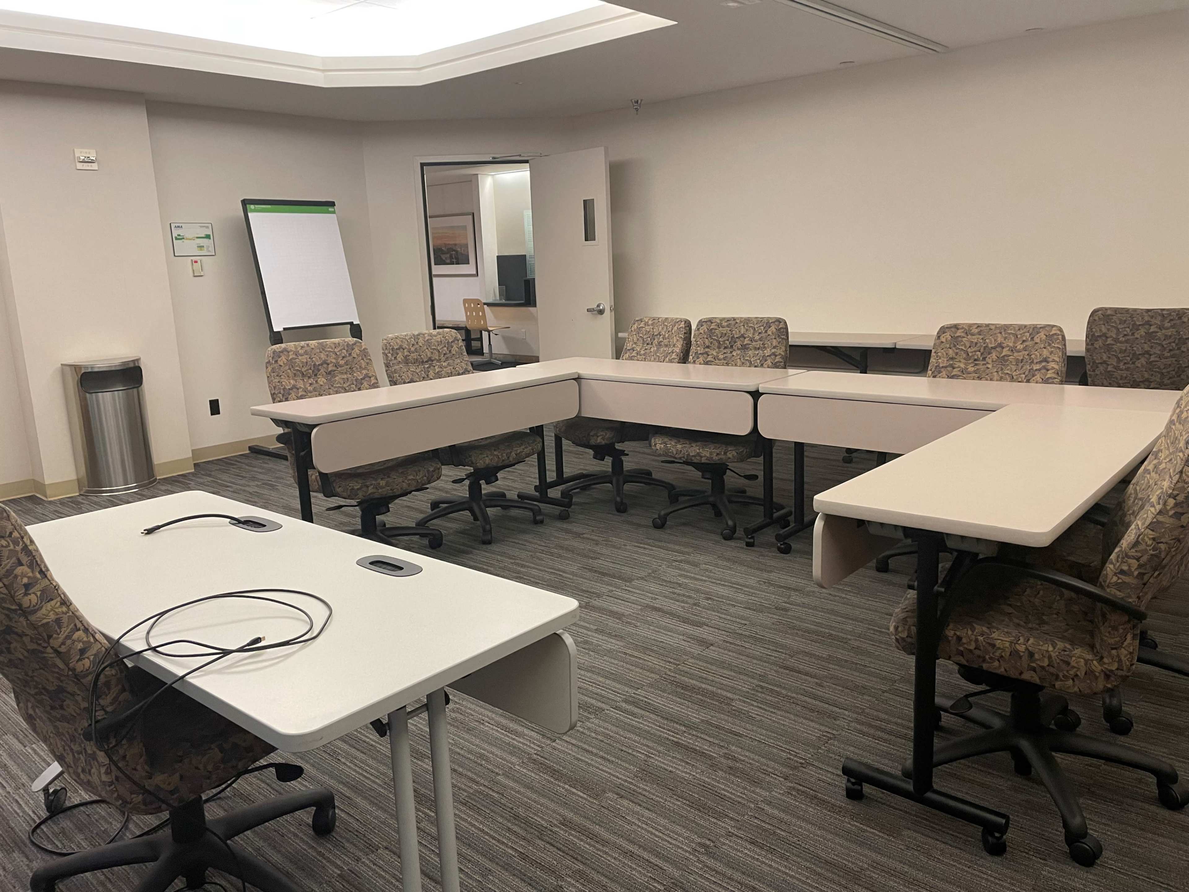 A meeting room with multiple tables arranged in a U-shape and several chairs surrounding them.