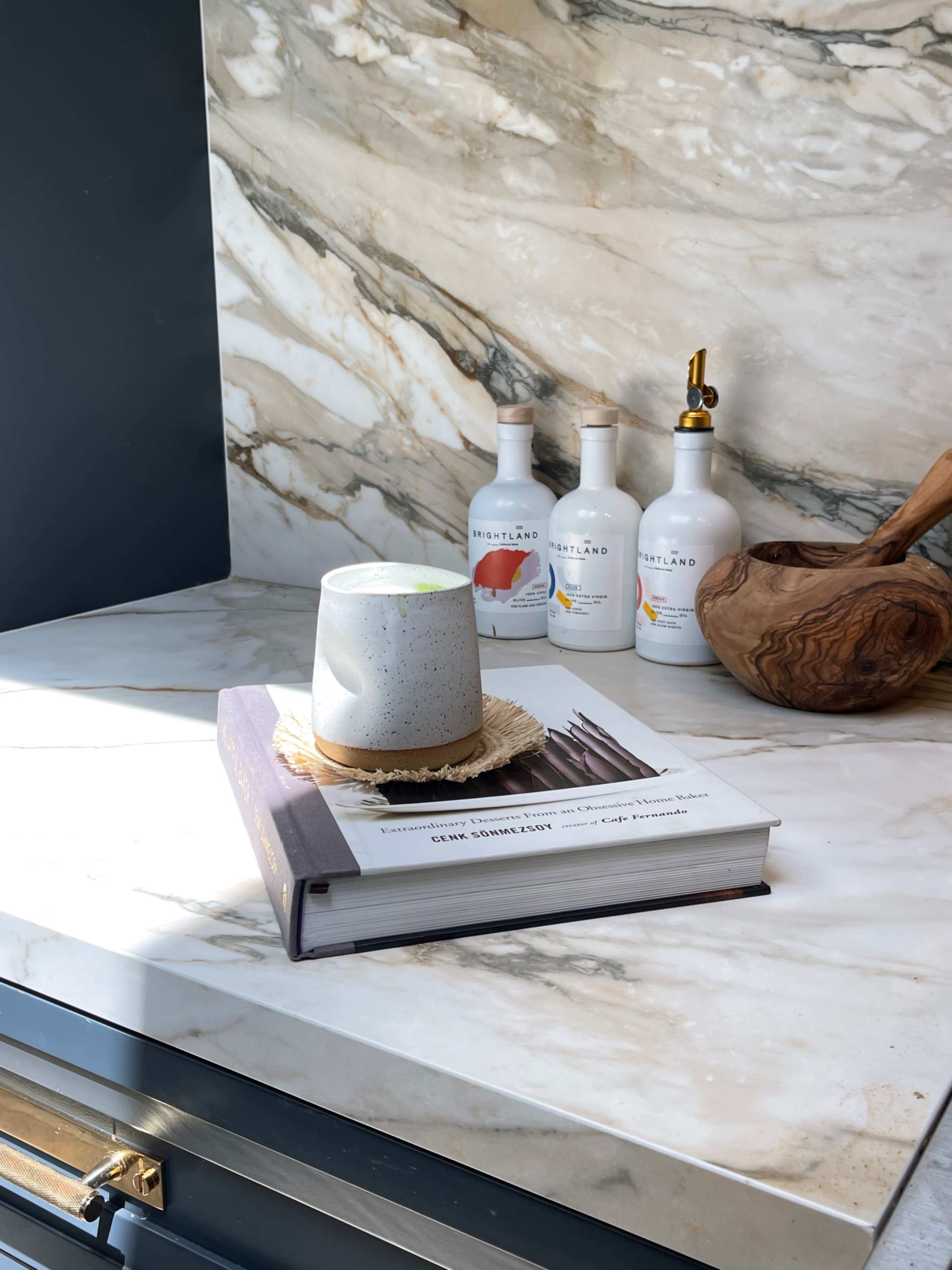 A concrete cup is placed on a book atop a marble countertop, with three bottles in the background.
