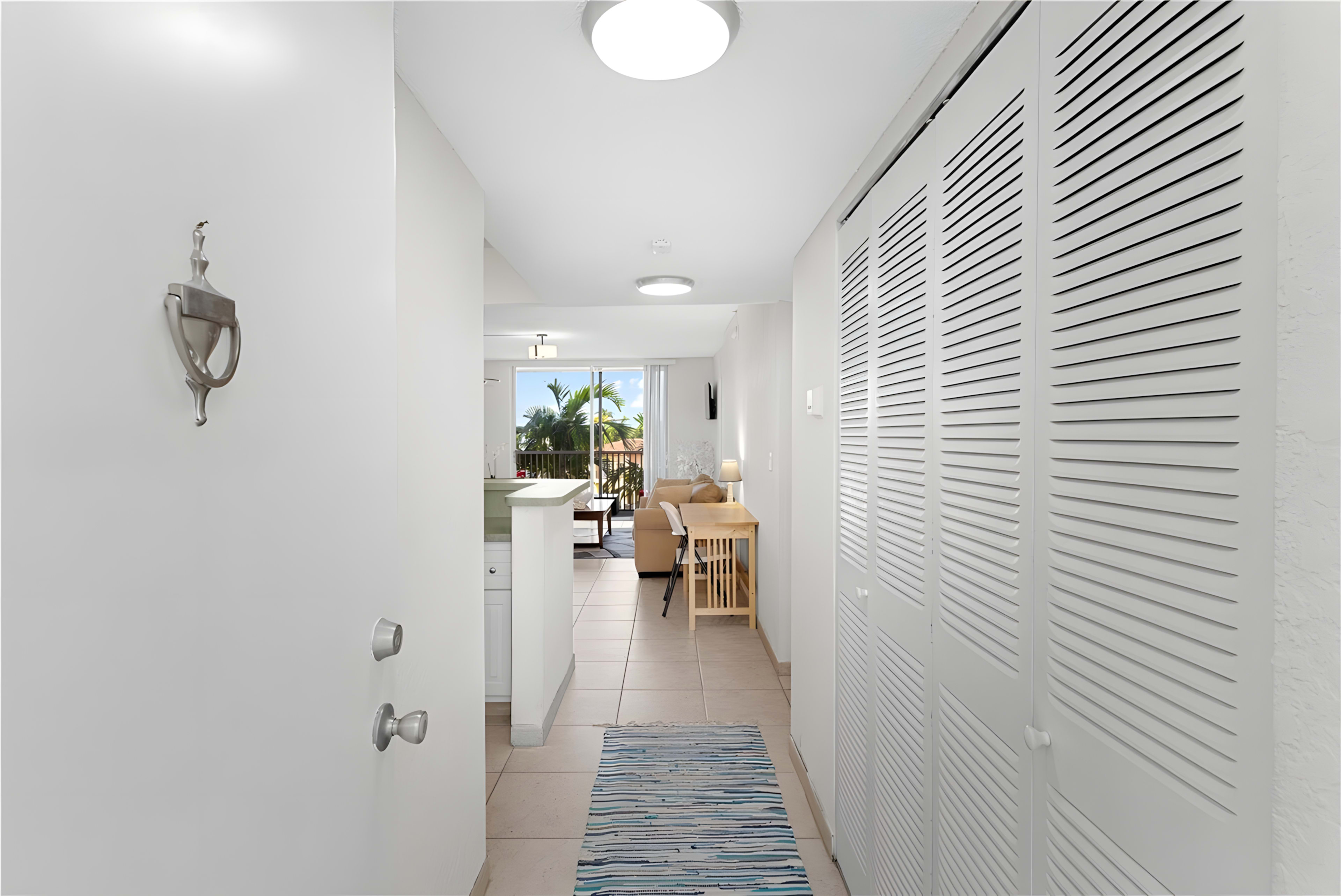 A hallway leads to an open living space with a view of palm trees outside.