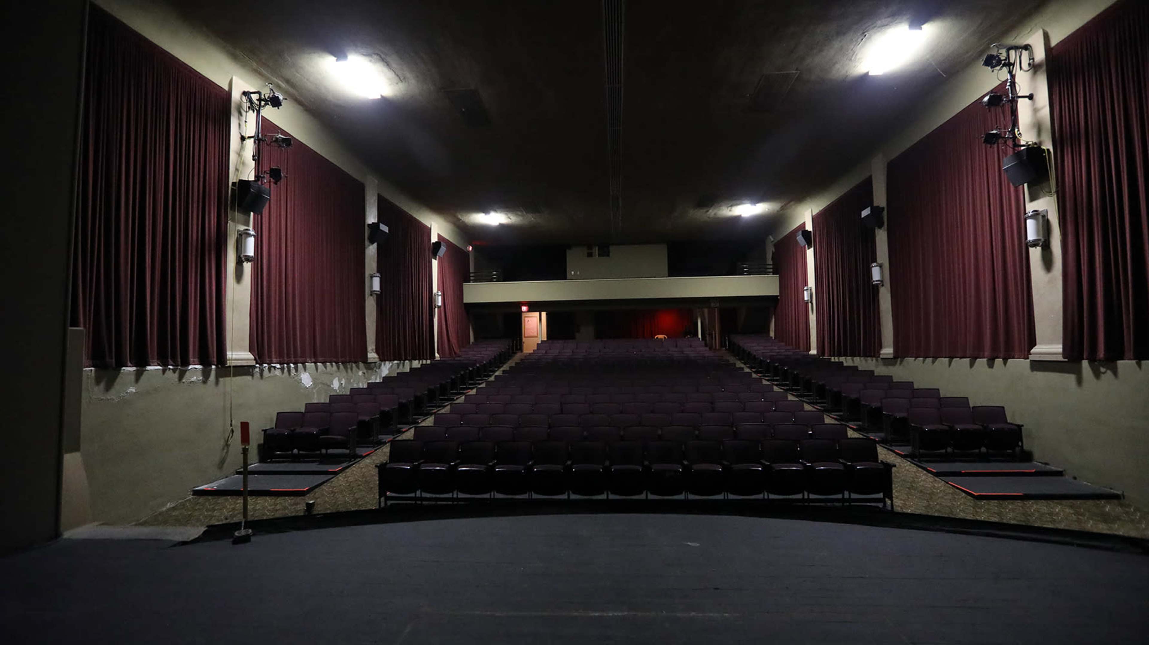 A dimly lit theater interior with rows of empty purple seats and red curtains on the walls.