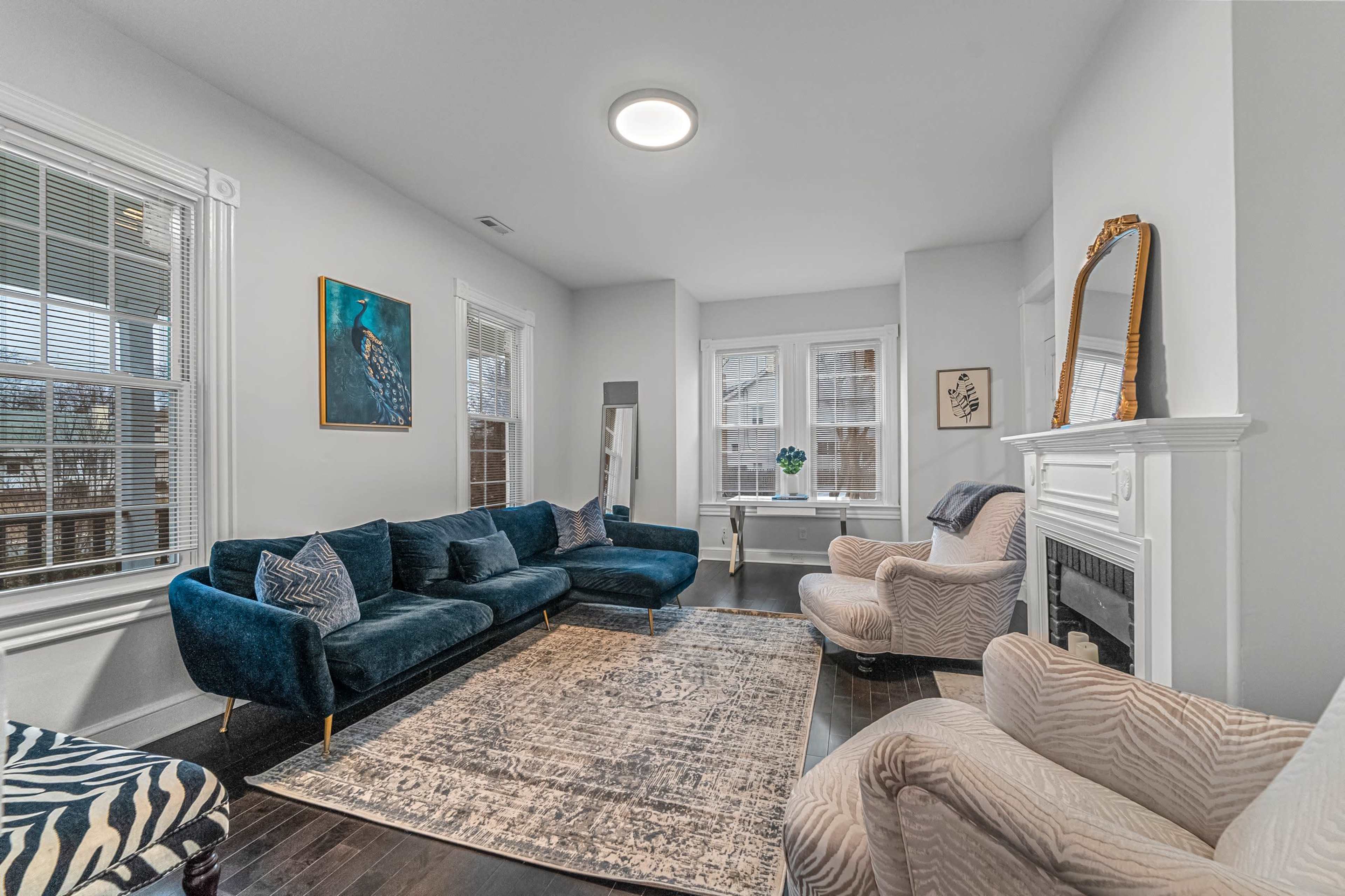 A modern living room with a large dark blue sectional sofa, two patterned armchairs, a coffee table, and a decorative rug under a window with natural light.