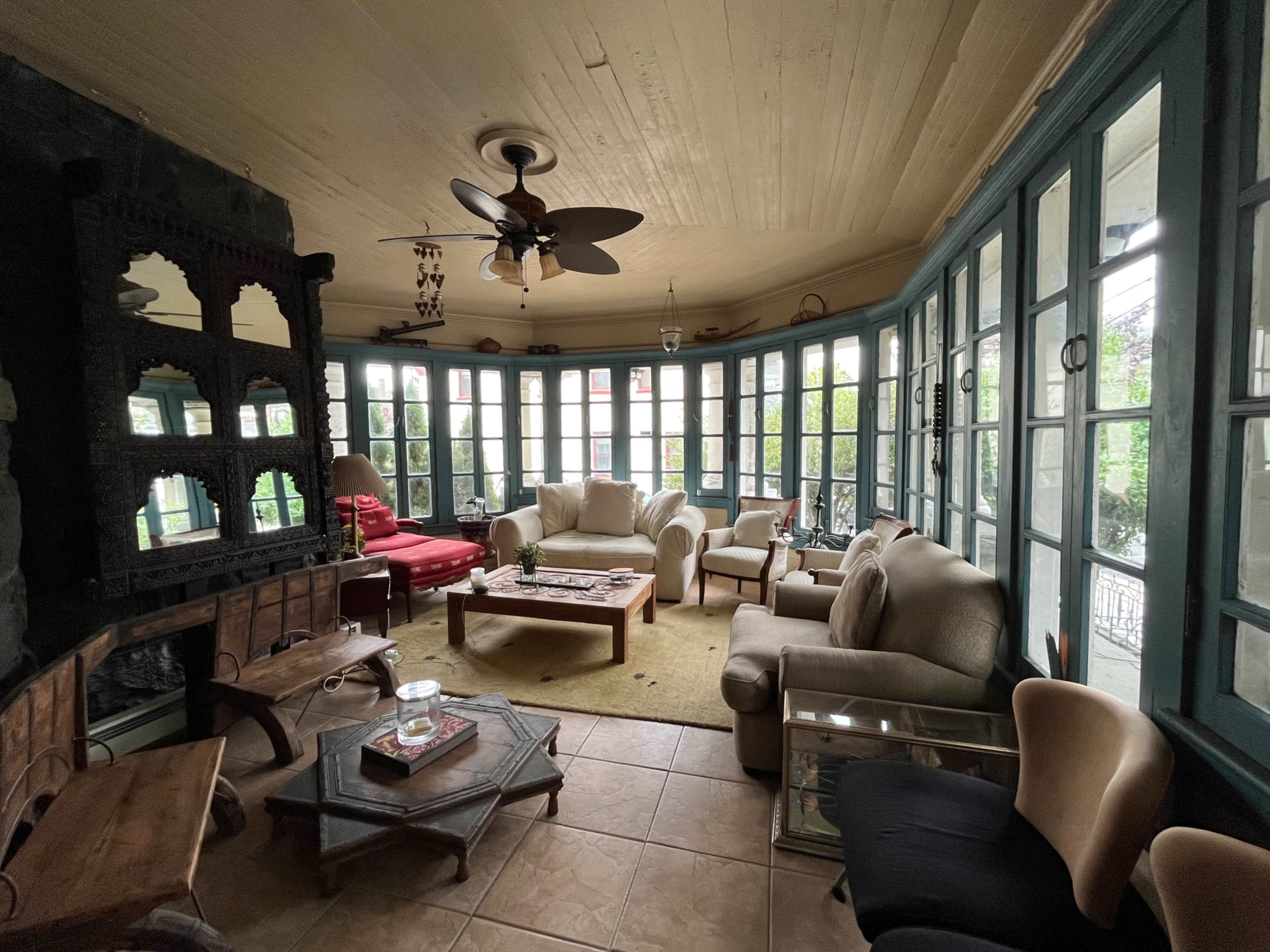 A sunroom filled with various seating arrangements, large windows, and a stone fireplace.