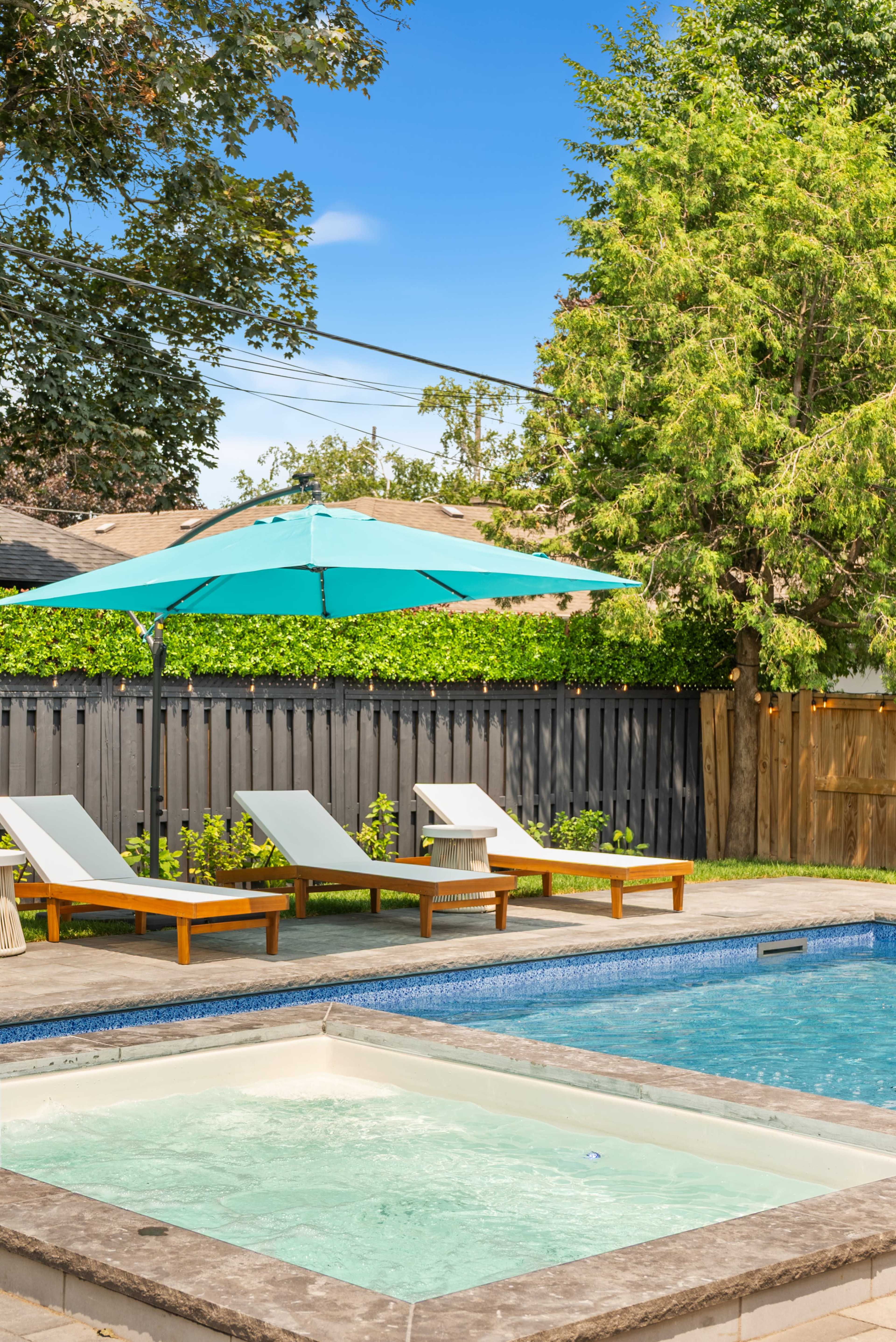 The image shows a backyard pool area featuring a large umbrella over two loungers beside a hot tub and a swimming pool.