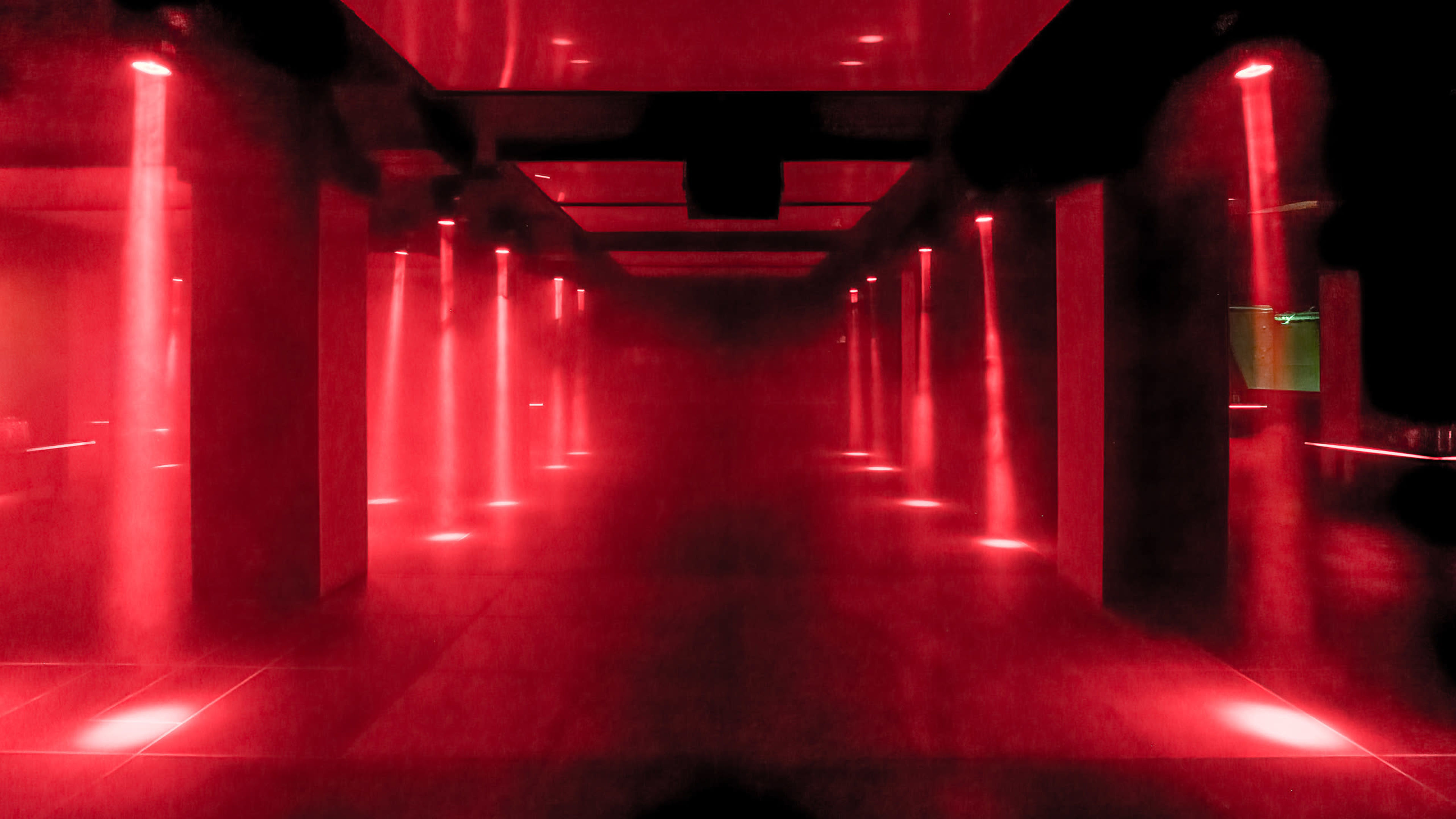 A dimly lit space with red lights casting vertical beams through a light mist.